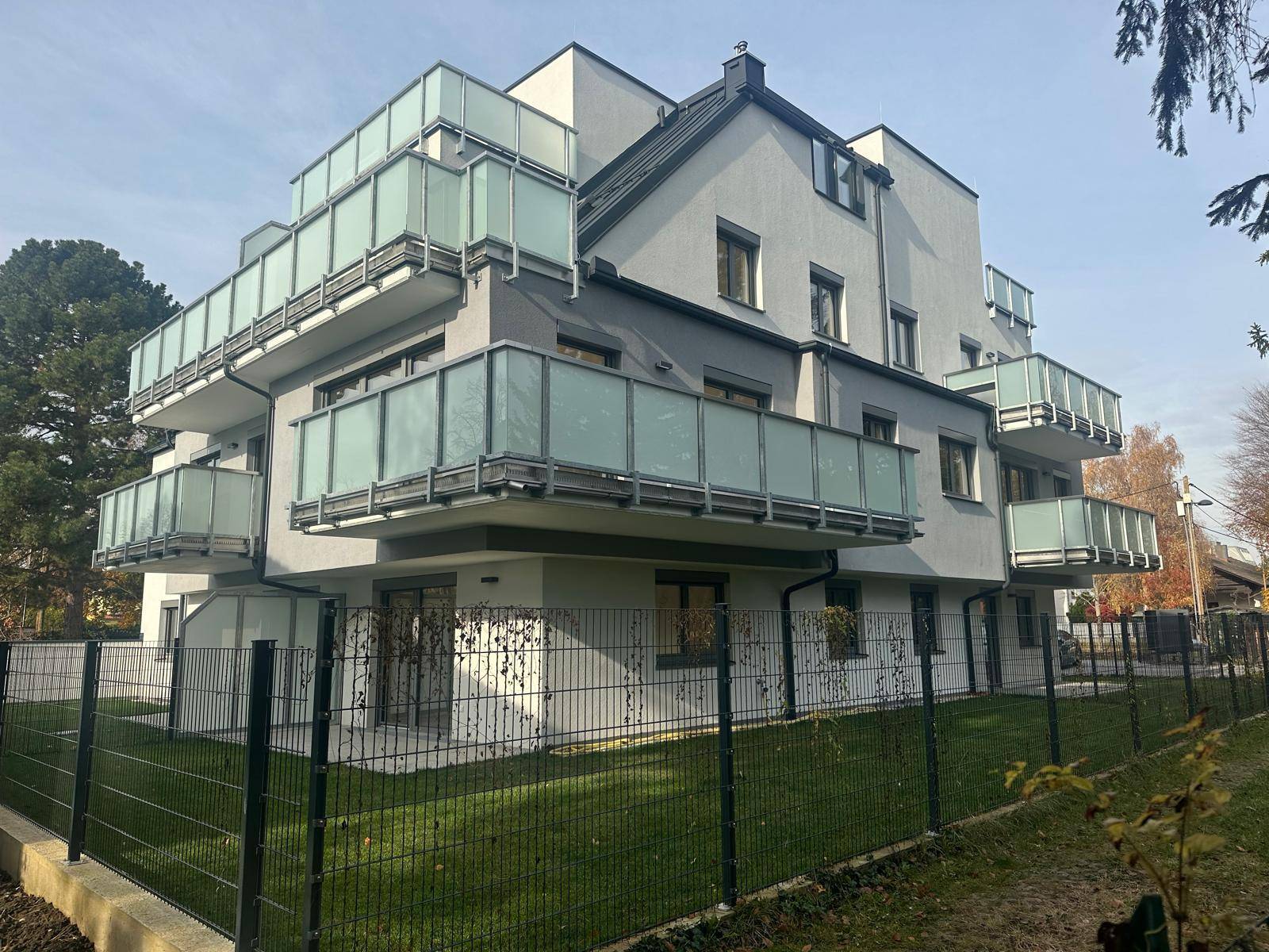 Seitenansicht des modernen Gebäudes mit Balkonen, Zaun und Rasenfläche.