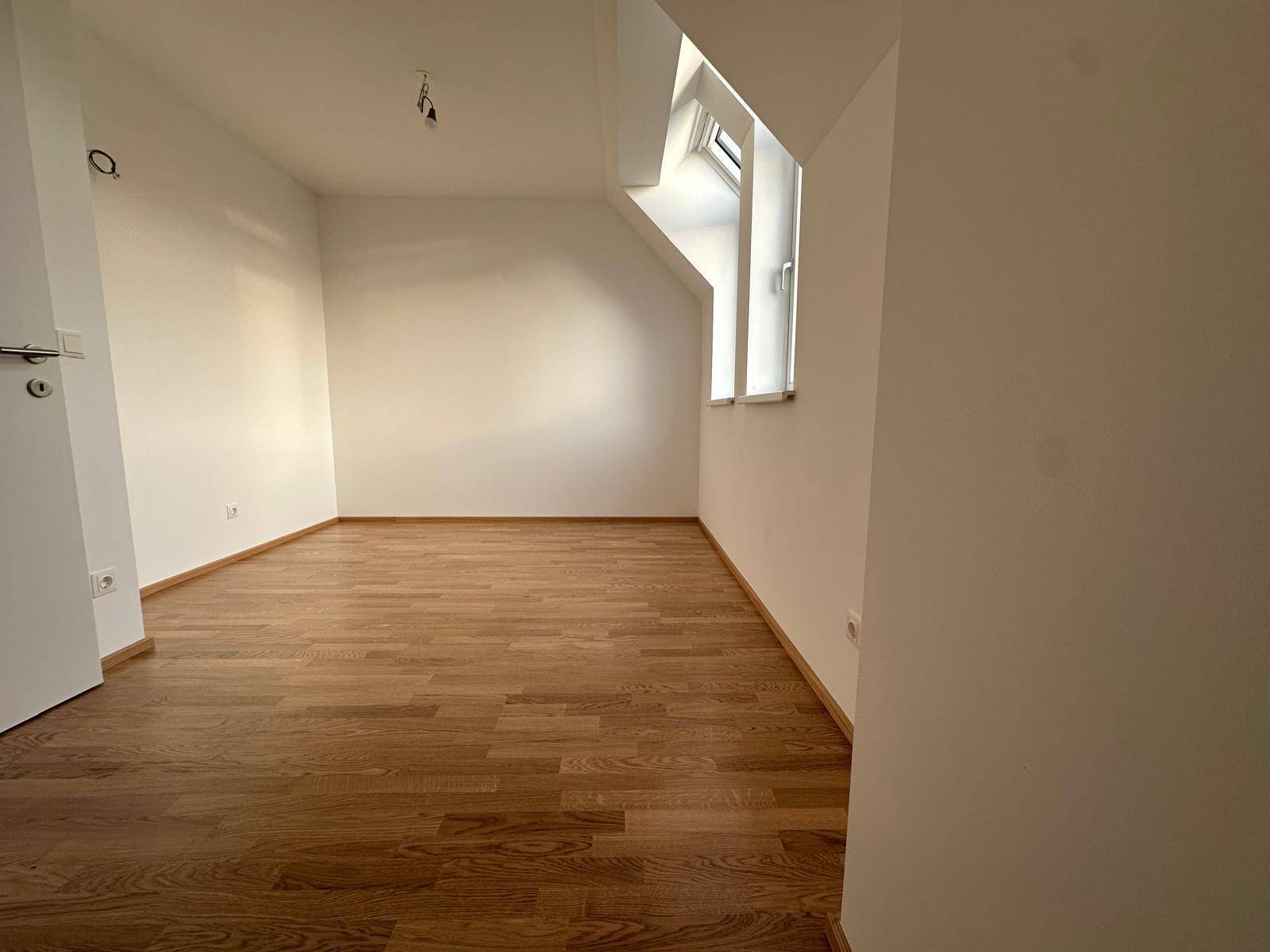 Helles Zimmer mit Parkettboden und Dachfenster, ideal als Schlaf- oder Arbeitszimmer.
