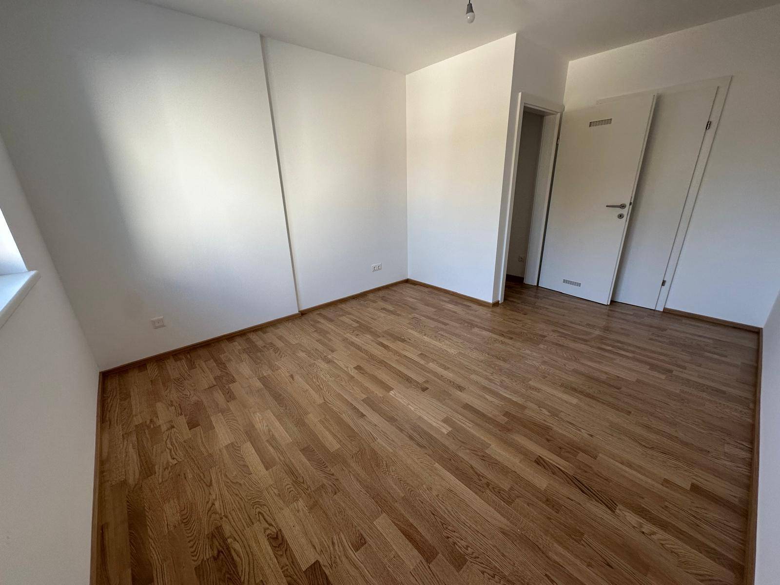Helles Schlafzimmer mit neuem Parkettboden und weiß gestrichenen Wänden.