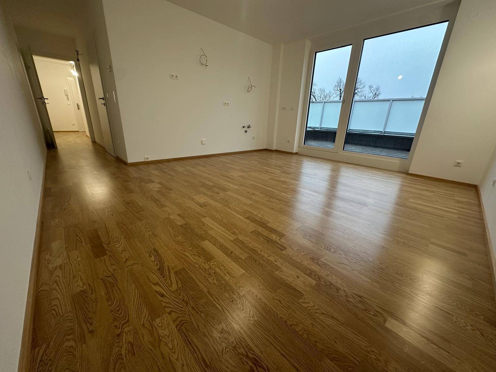 Geräumiges Wohnzimmer mit Holzboden, großen Fenstern und Zugang zu einem Außenbereich.