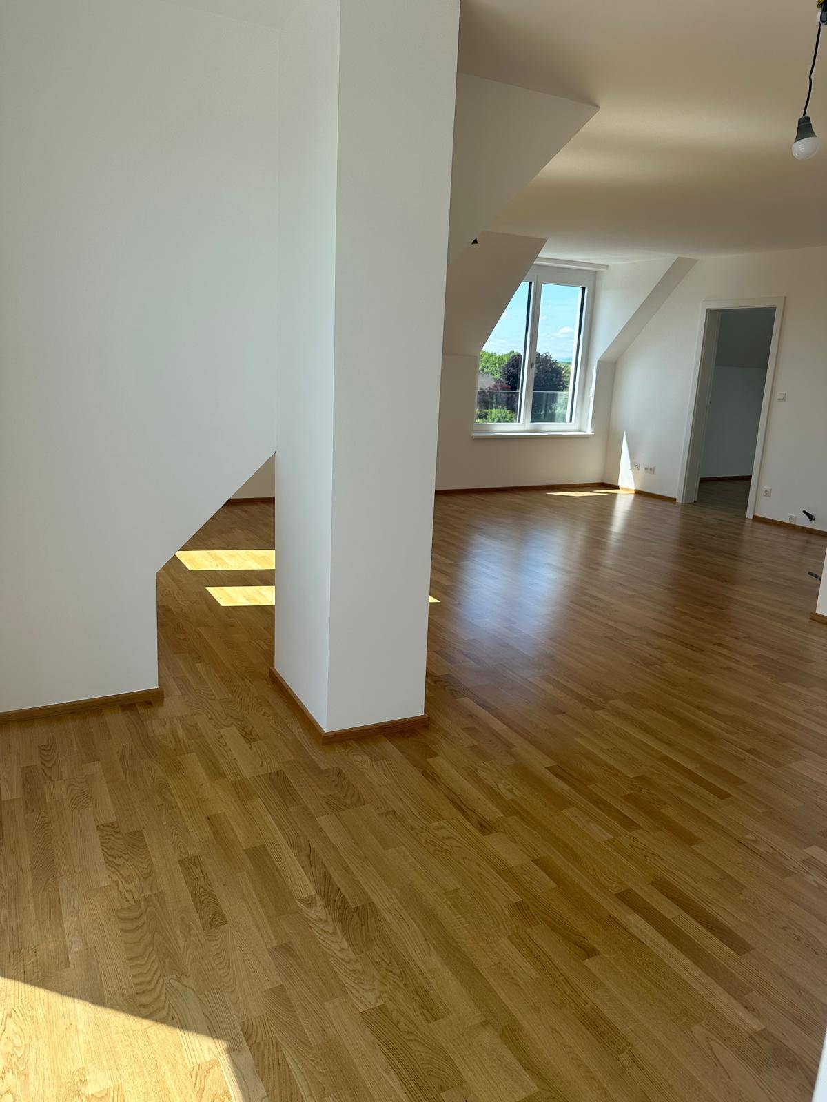 Heller Wohnbereich mit Parkettboden, weißen Wänden und viel Tageslicht.