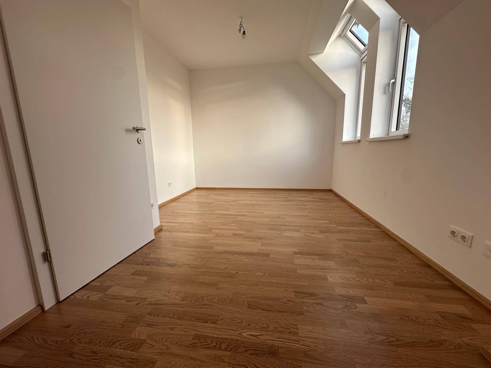 Leeres Schlafzimmer mit Holzboden, Dachschräge und einem Fenster für natürliches Licht.