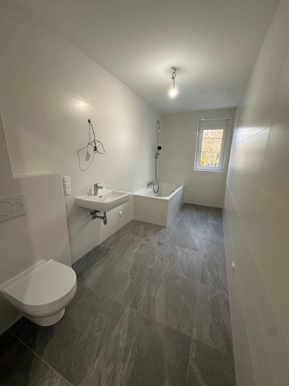 Modernes Badezimmer mit Badewanne, WC, Waschbecken und Fenster für Tageslicht.