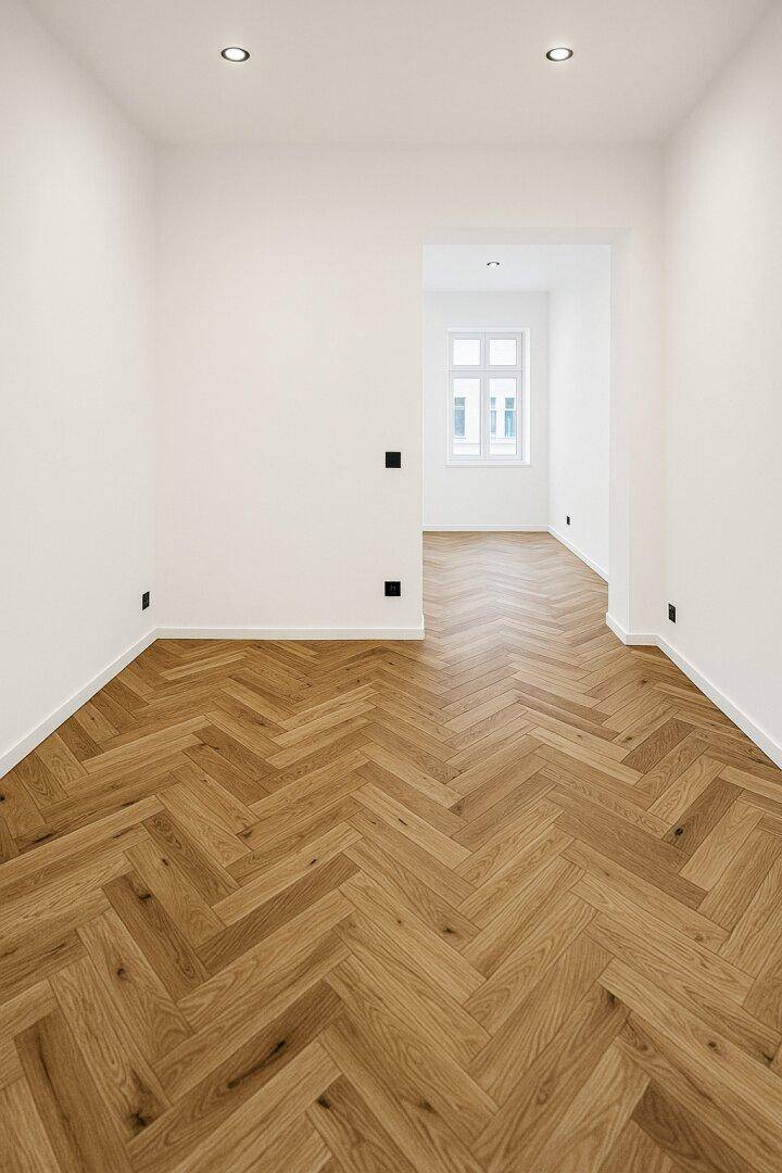 Heller Flur mit Fischgrätparkett und Blick in einen weiteren Raum.