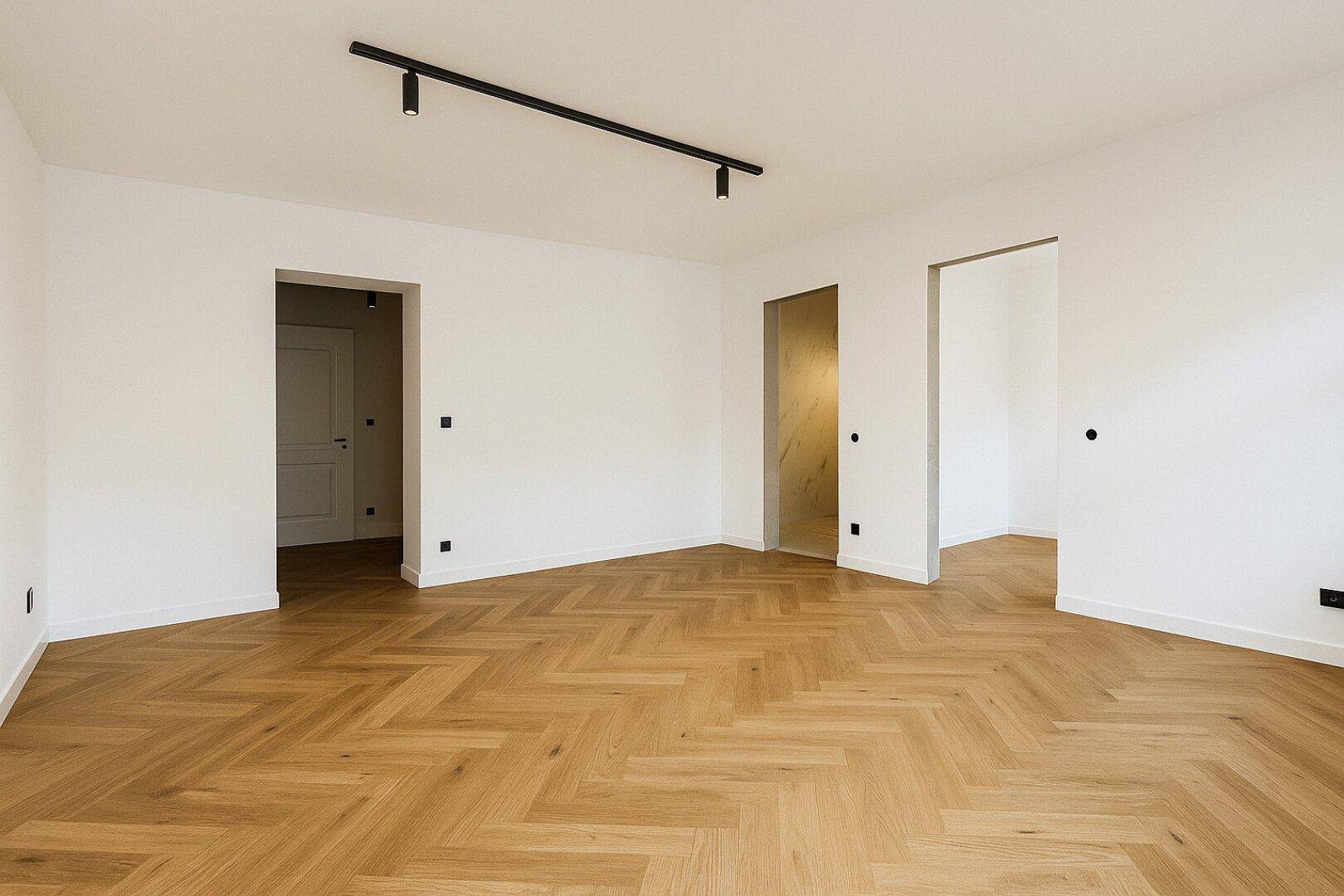 Geräumiges Zimmer mit Fischgrätparkett und Zugang zu weiteren Räumen.
