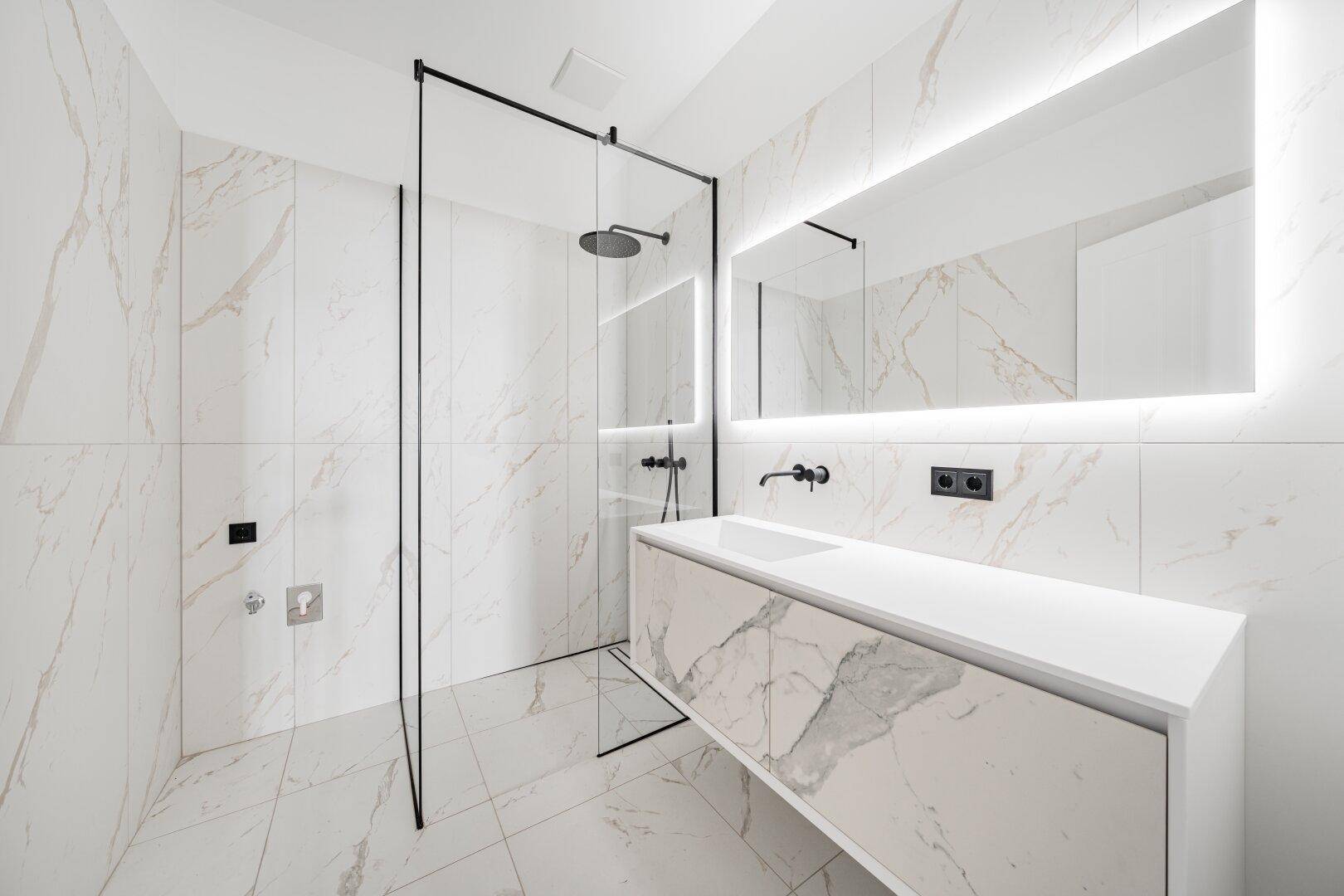 Modernes Badezimmer mit Marmorfliesen, begehbarer Dusche und beleuchtetem Spiegel.