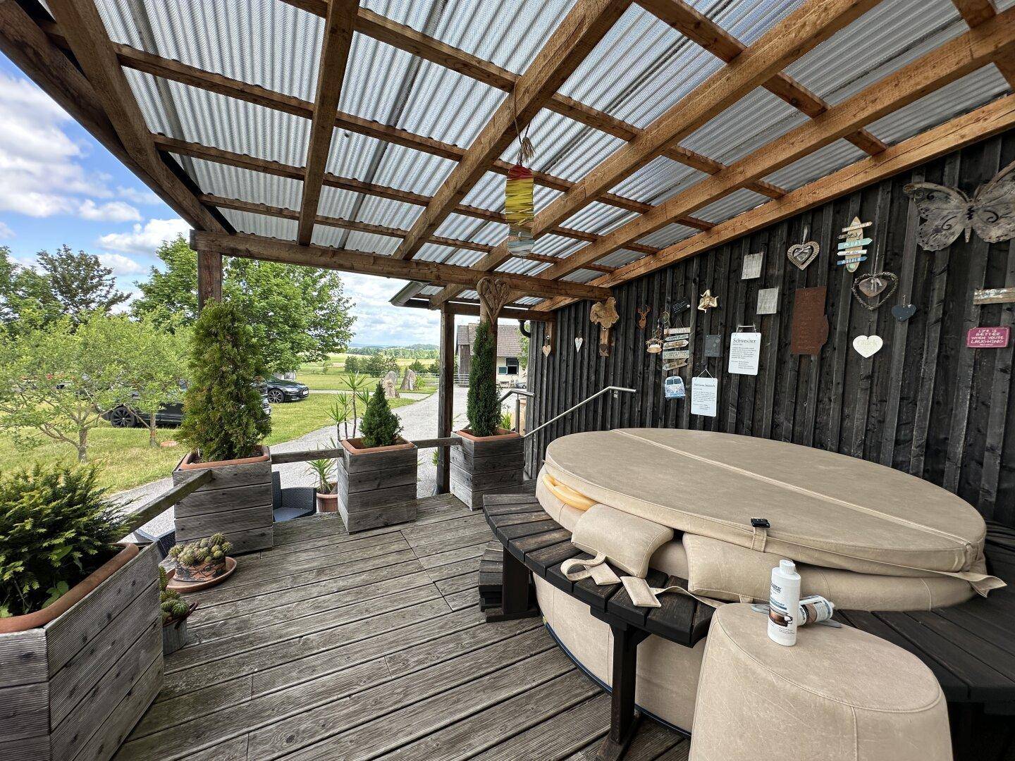 Überdachte Holzterrasse mit einem Whirlpool und Blick auf die umliegende Landschaft.