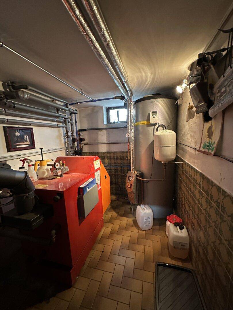 Heizungsraum im Keller mit Kessel, Warmwasserspeicher und sichtbaren Rohren.