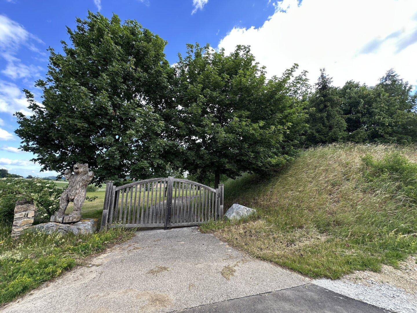 Rustikales Holztor umgeben von Bäumen und Gras, das den Eingang zum Anwesen markiert.