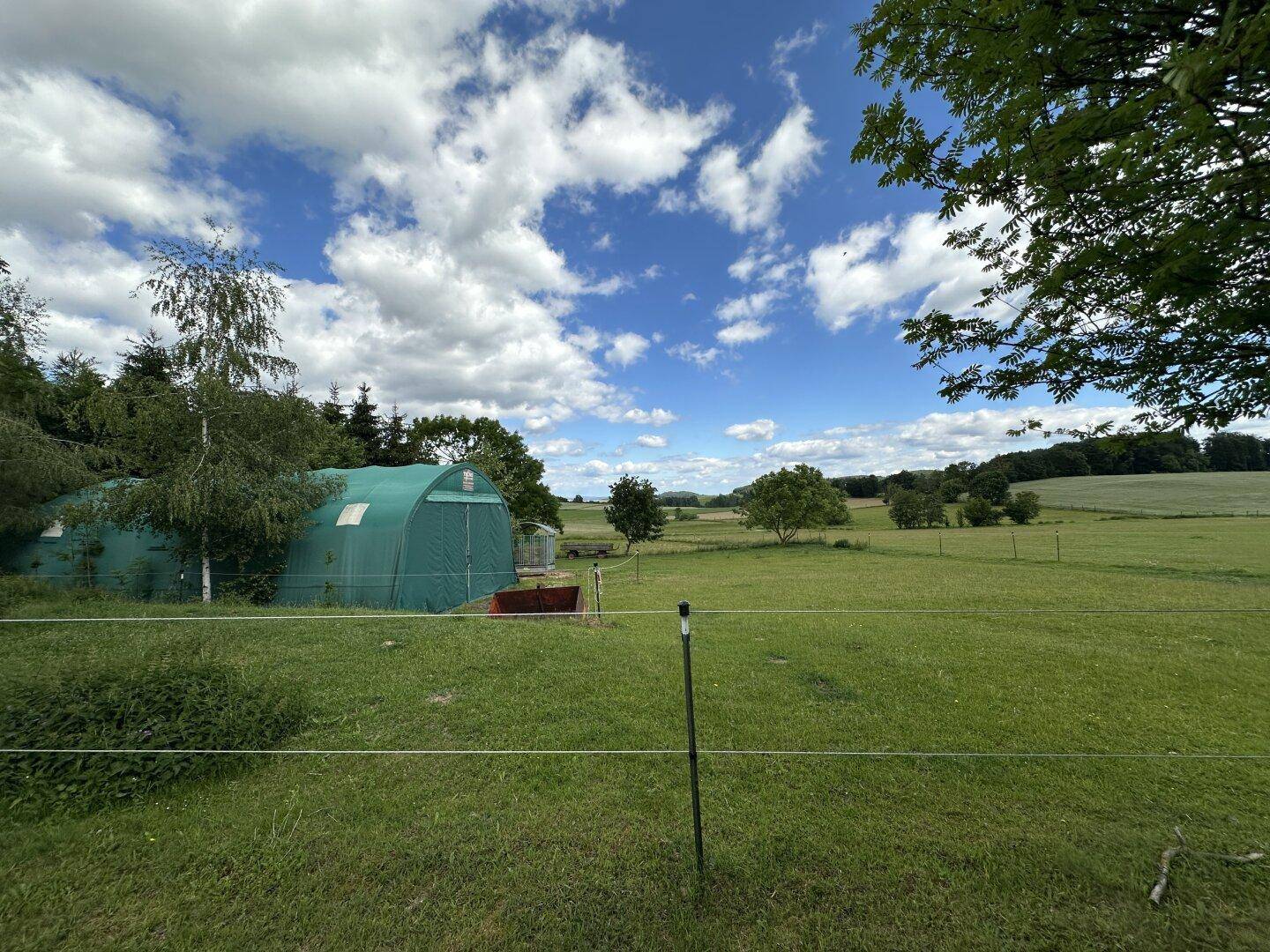 Ländliche Landschaft mit grüner Zeltstruktur und weiten Feldern unter bewölktem Himmel.