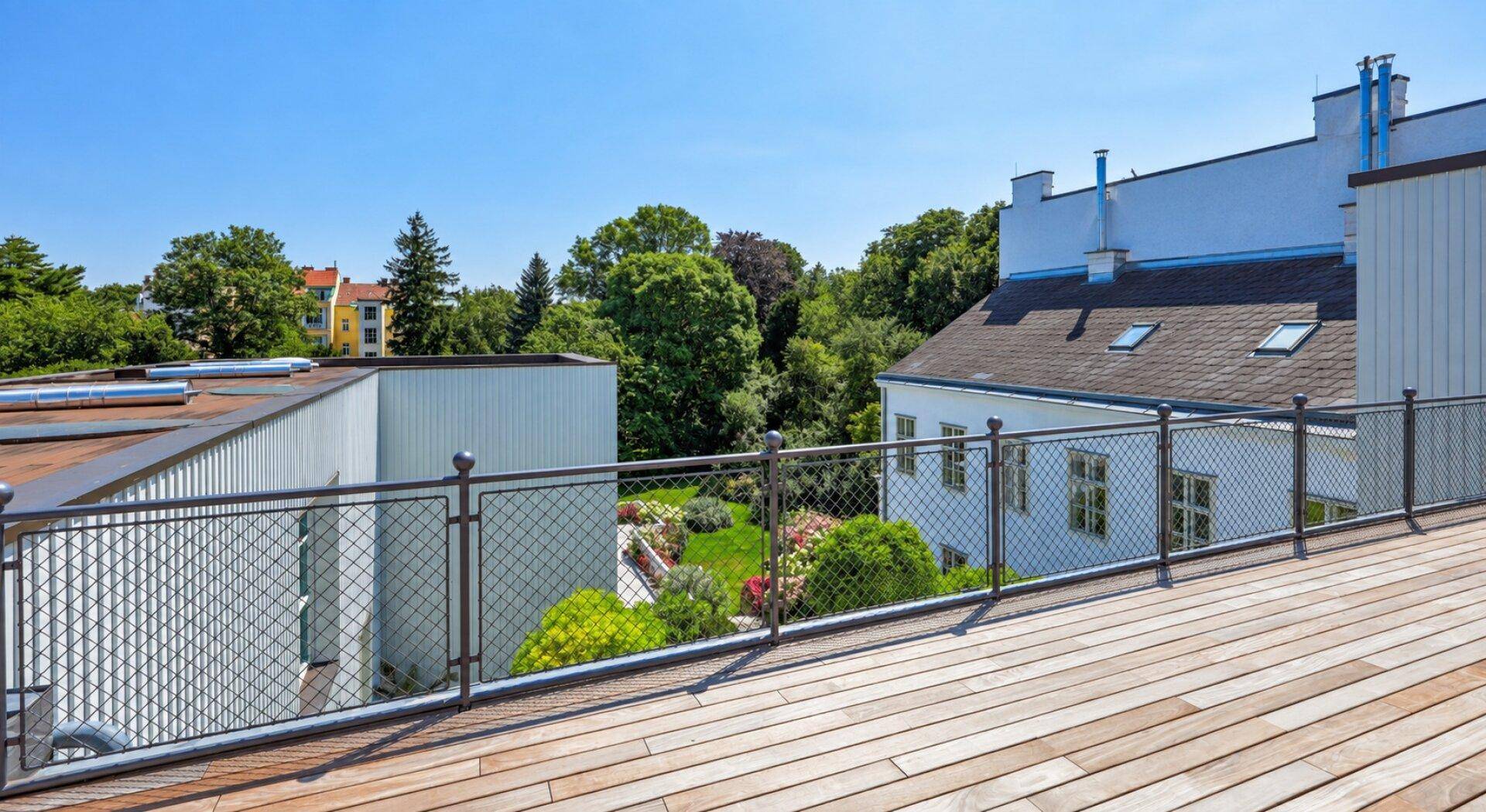 Weitläufige Holzterrasse mit Metallgeländer und Blick auf den grünen Gartenbereich.