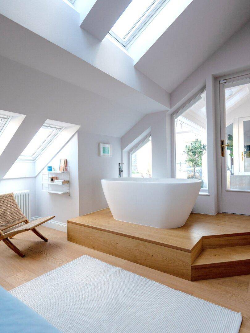 Luxuriöses Badezimmer mit freistehender Badewanne auf Podest, Dachfenstern und Holzboden.