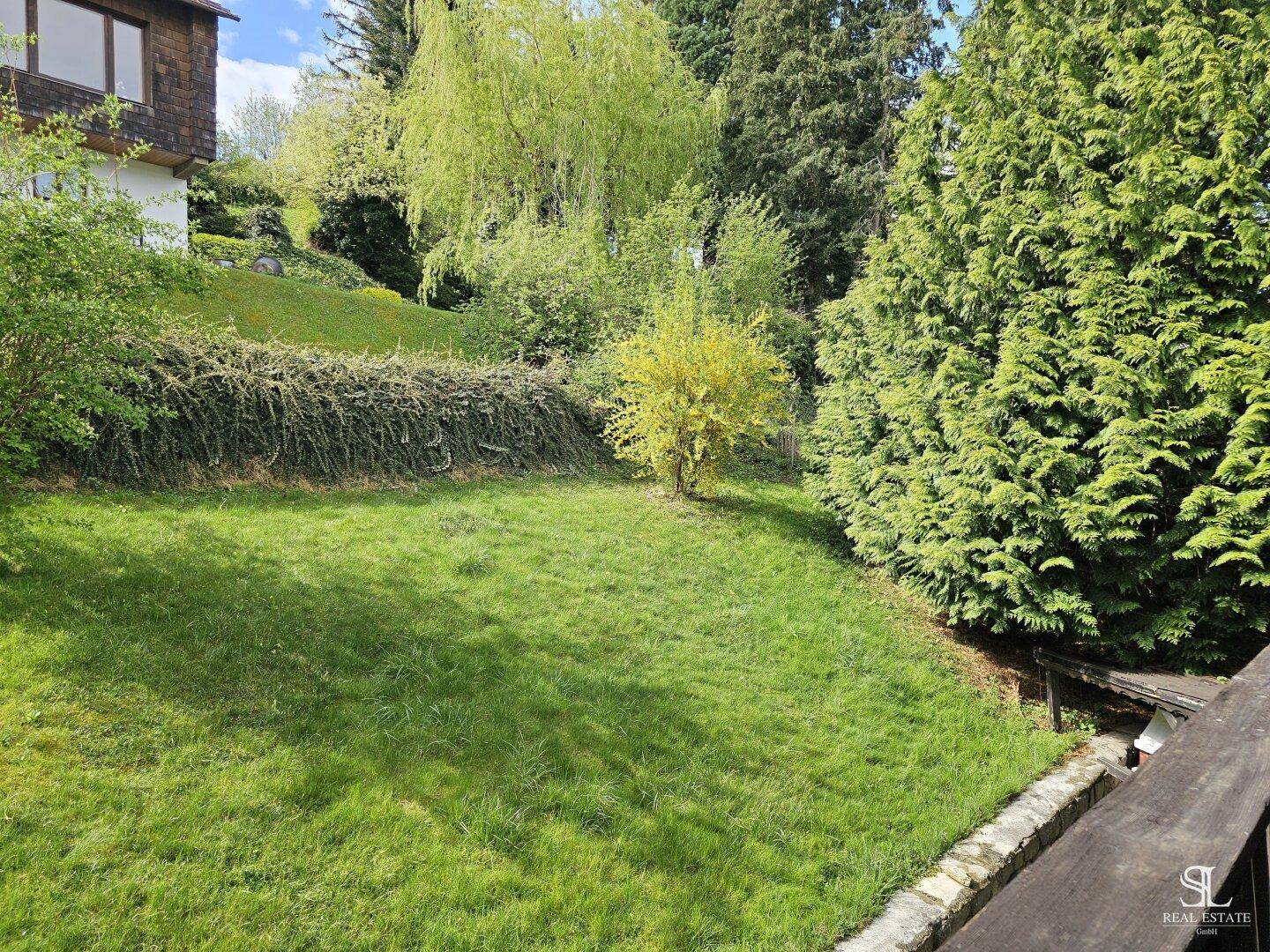 Weitläufiger grüner Garten mit Rasen und verschiedenen Bäumen unter blauem Himmel.