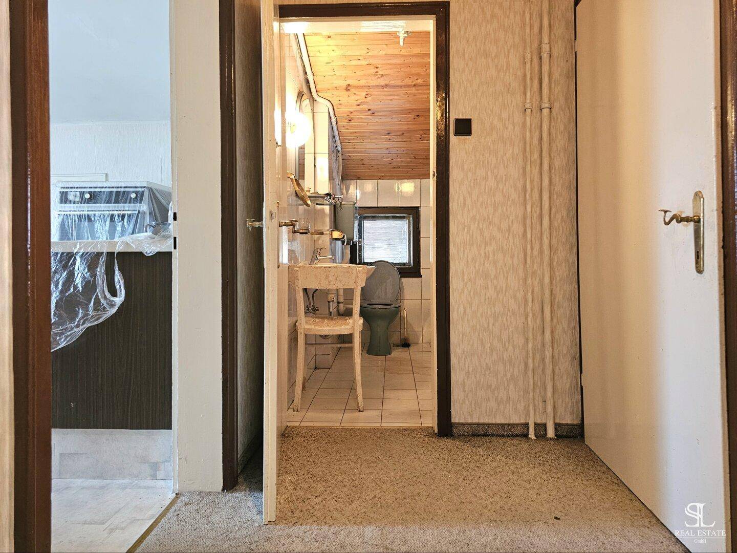 Kleines Badezimmer mit Waschbecken, Toilette, Fenster und Holzdecke im älteren Stil.
