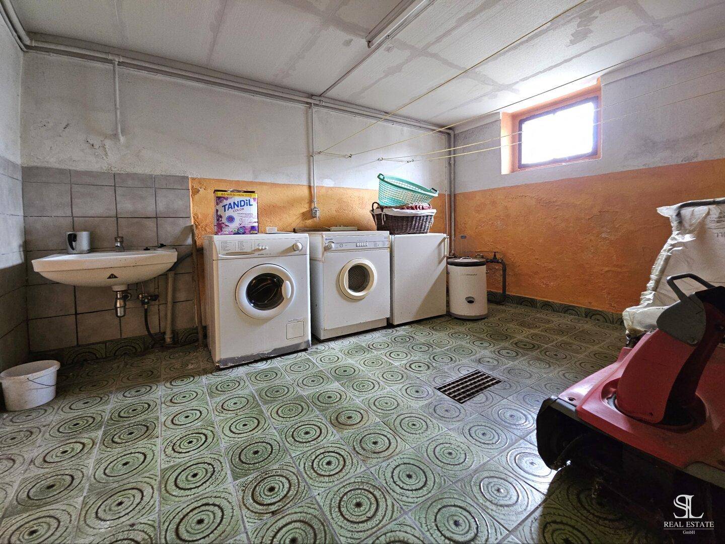 Waschküche im Keller mit Waschmaschinen, Waschbecken und gefliestem Boden.