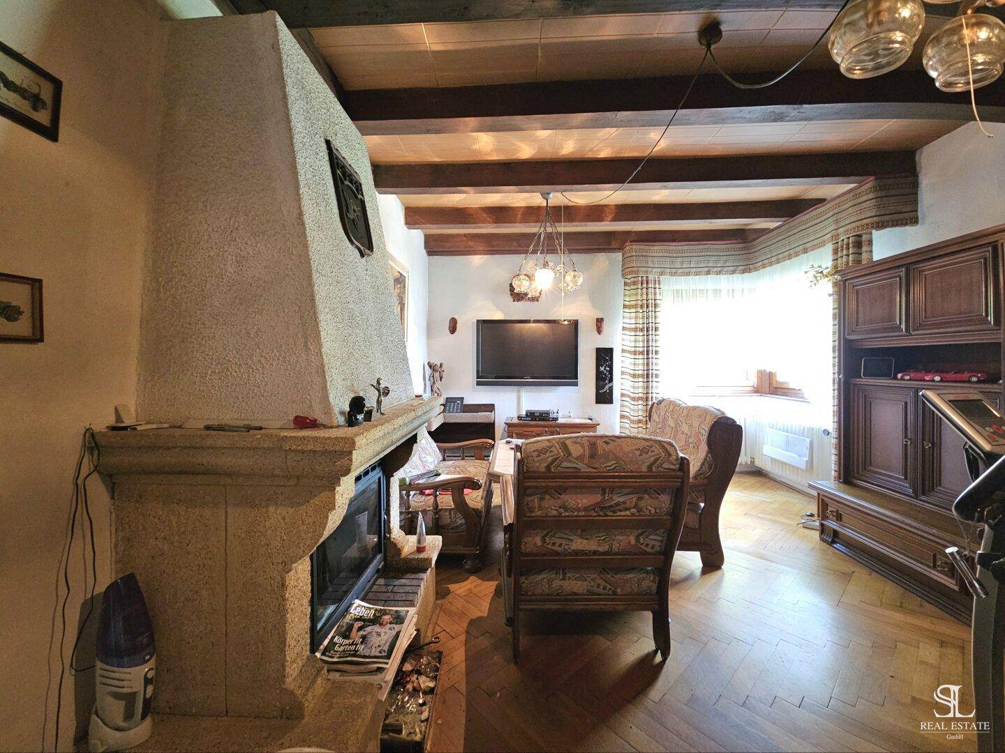 Gemütliches Wohnzimmer mit Kamin, Holzbalken an der Decke und Parkettboden.