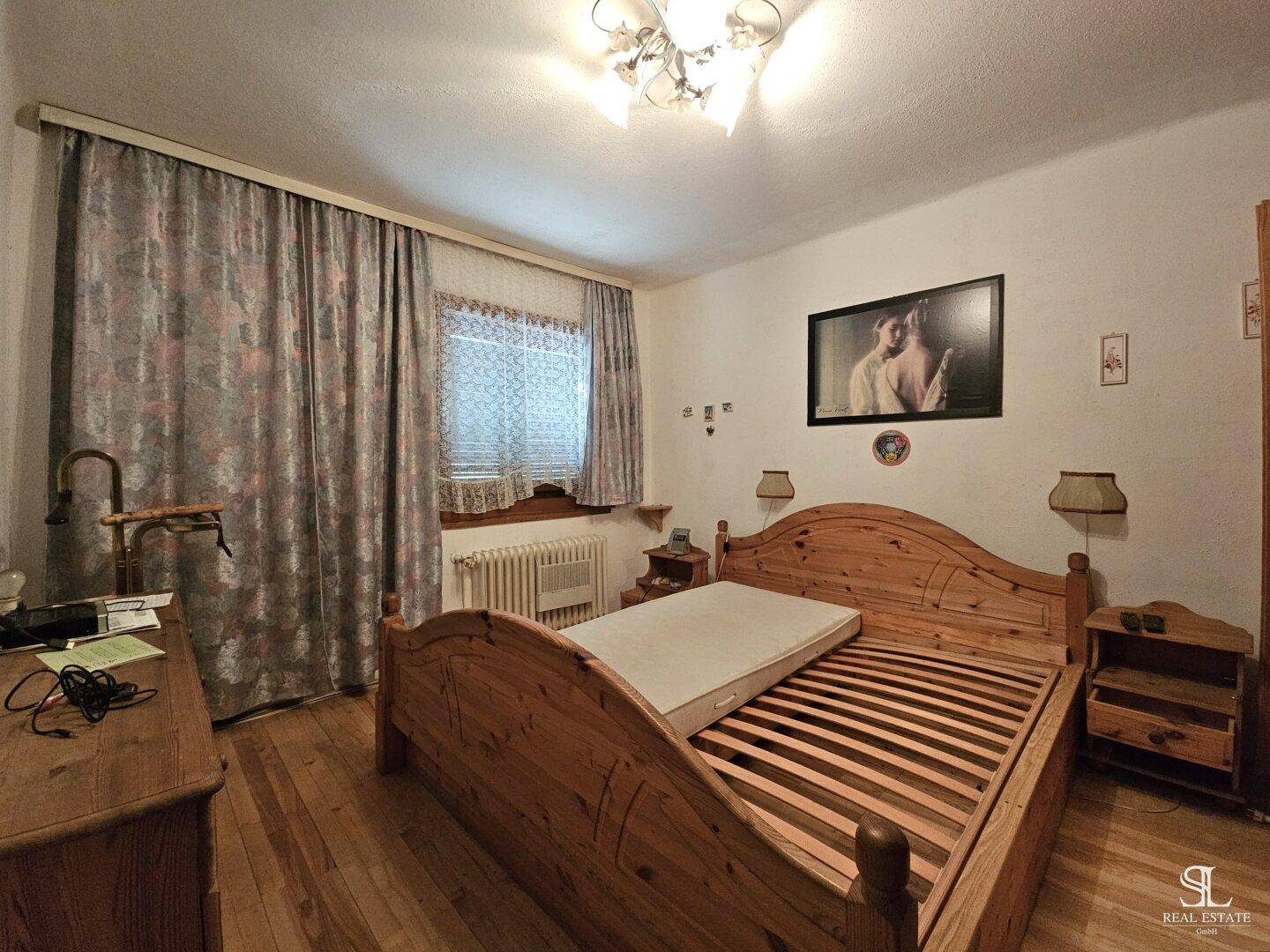 Schlafzimmer mit Holzboden, Doppelbett und großem Fenster mit Vorhängen.