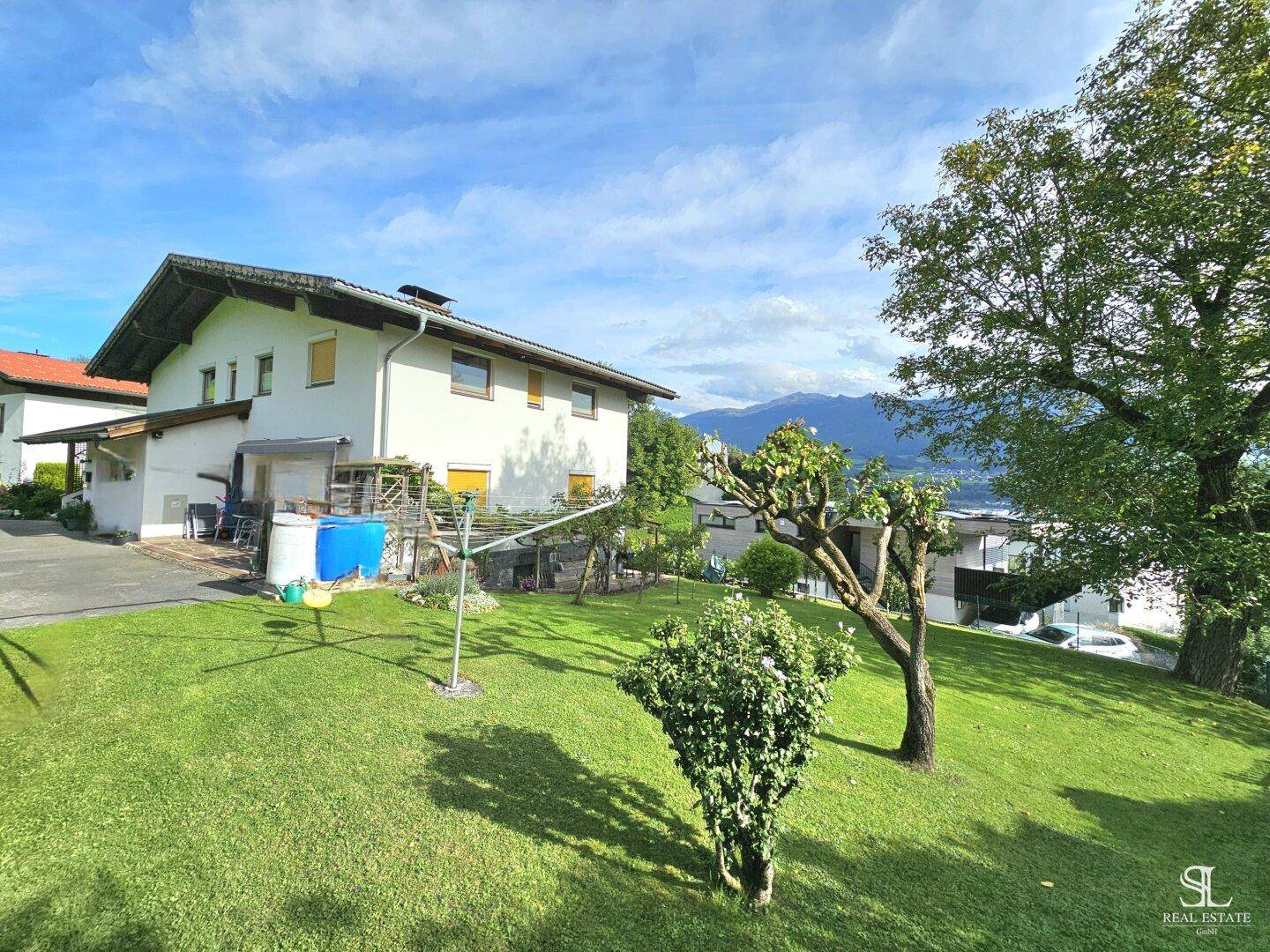 Großer, gepflegter Garten mit Rasenfläche und Blick auf die Rückseite des Hauses unter blauem Himmel.