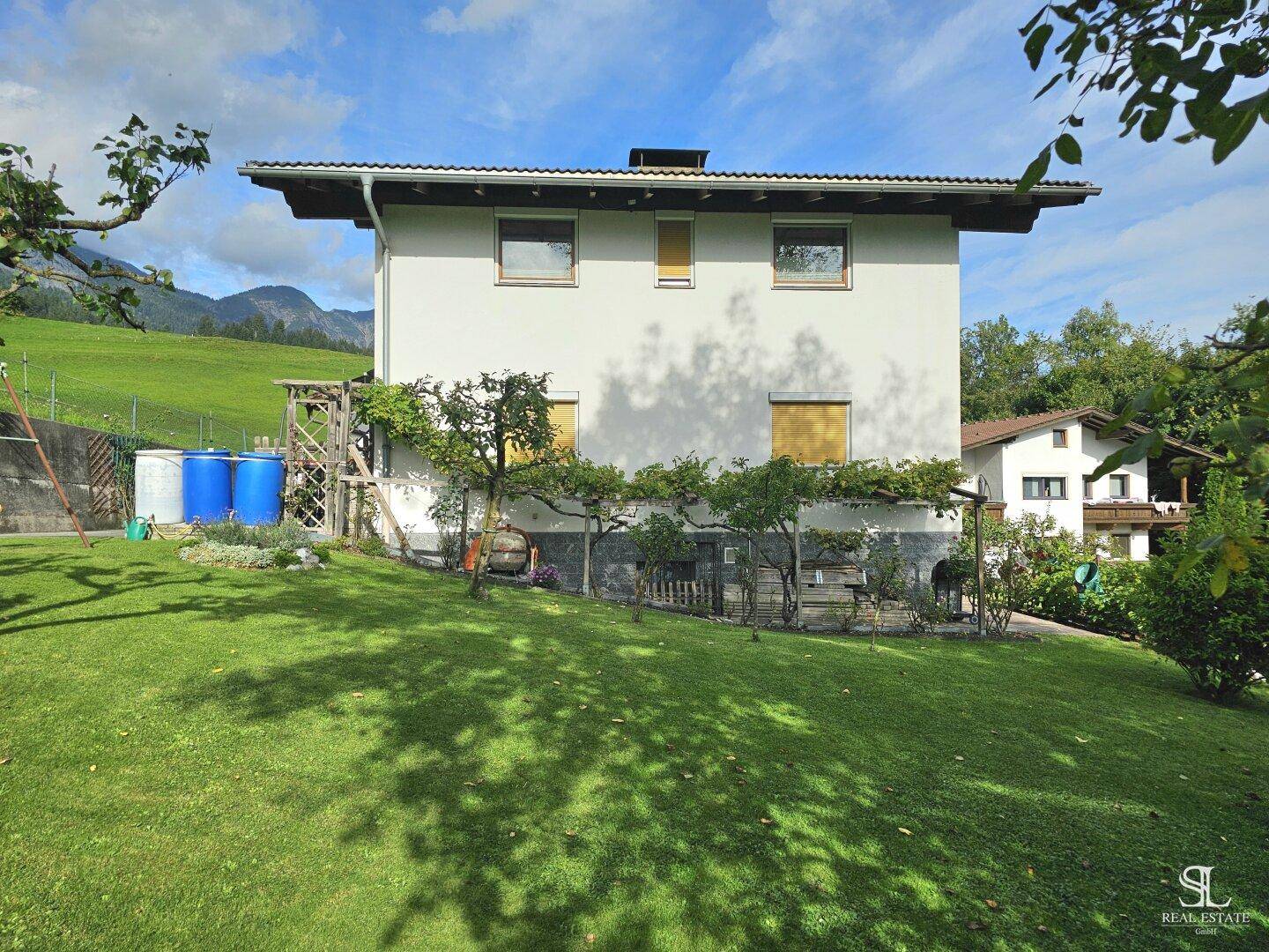 Rückansicht des Hauses mit großem, sonnigen Garten und grüner Rasenfläche.