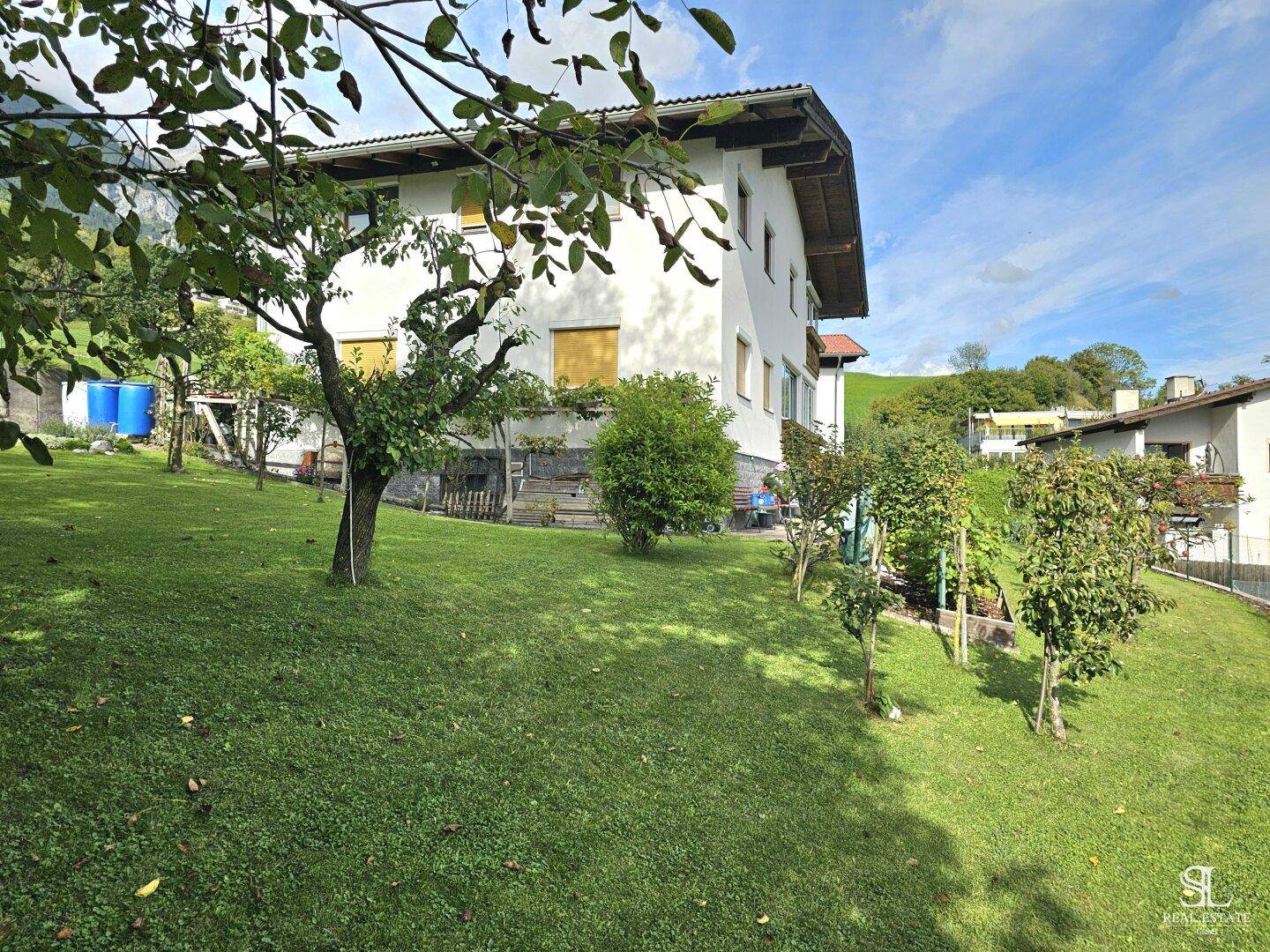Weitläufiger Gartenbereich mit Rasen, jungen Bäumen und der Seitenansicht des Hauses.