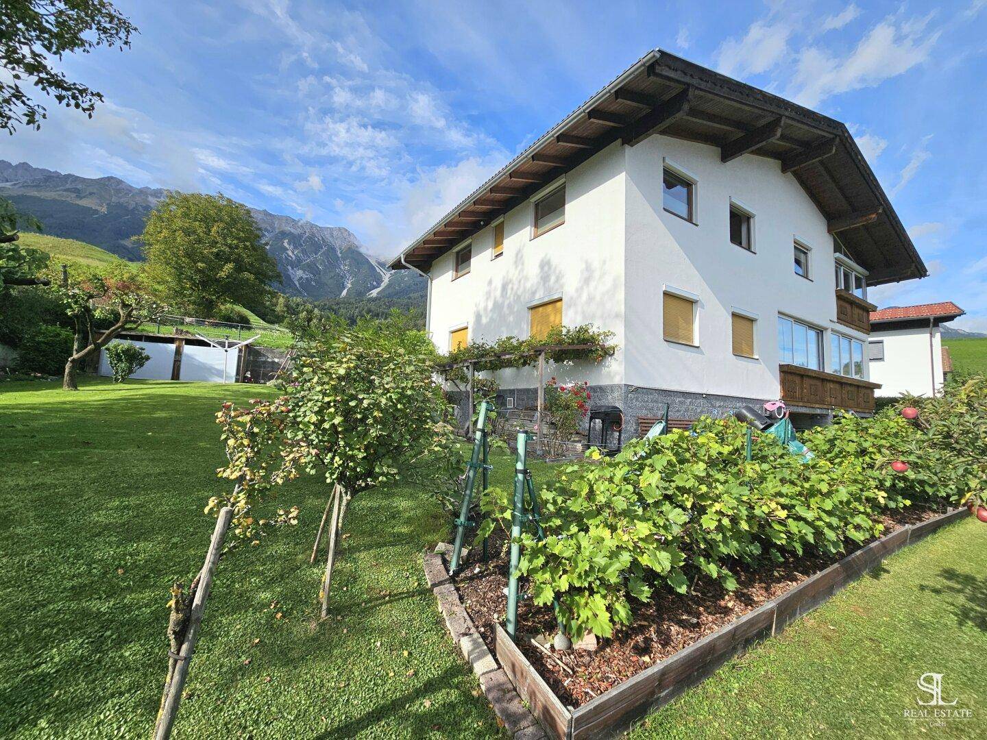 Sonnige Gartenseite des Hauses mit Hochbeeten und Blick auf die umliegende Natur.