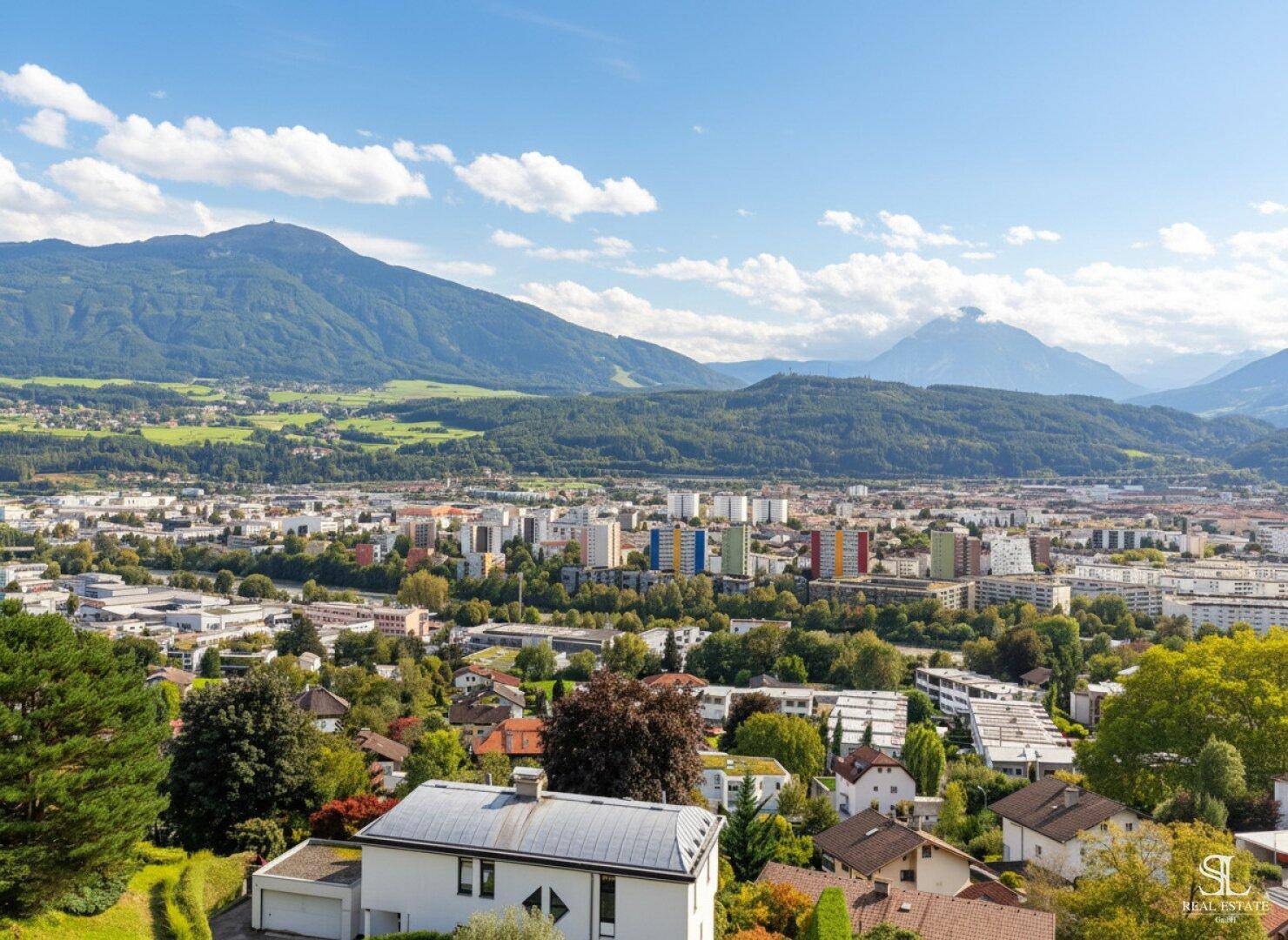 Weitläufiger Blick über die Stadt und die umliegende Berglandschaft unter blauem Himmel.