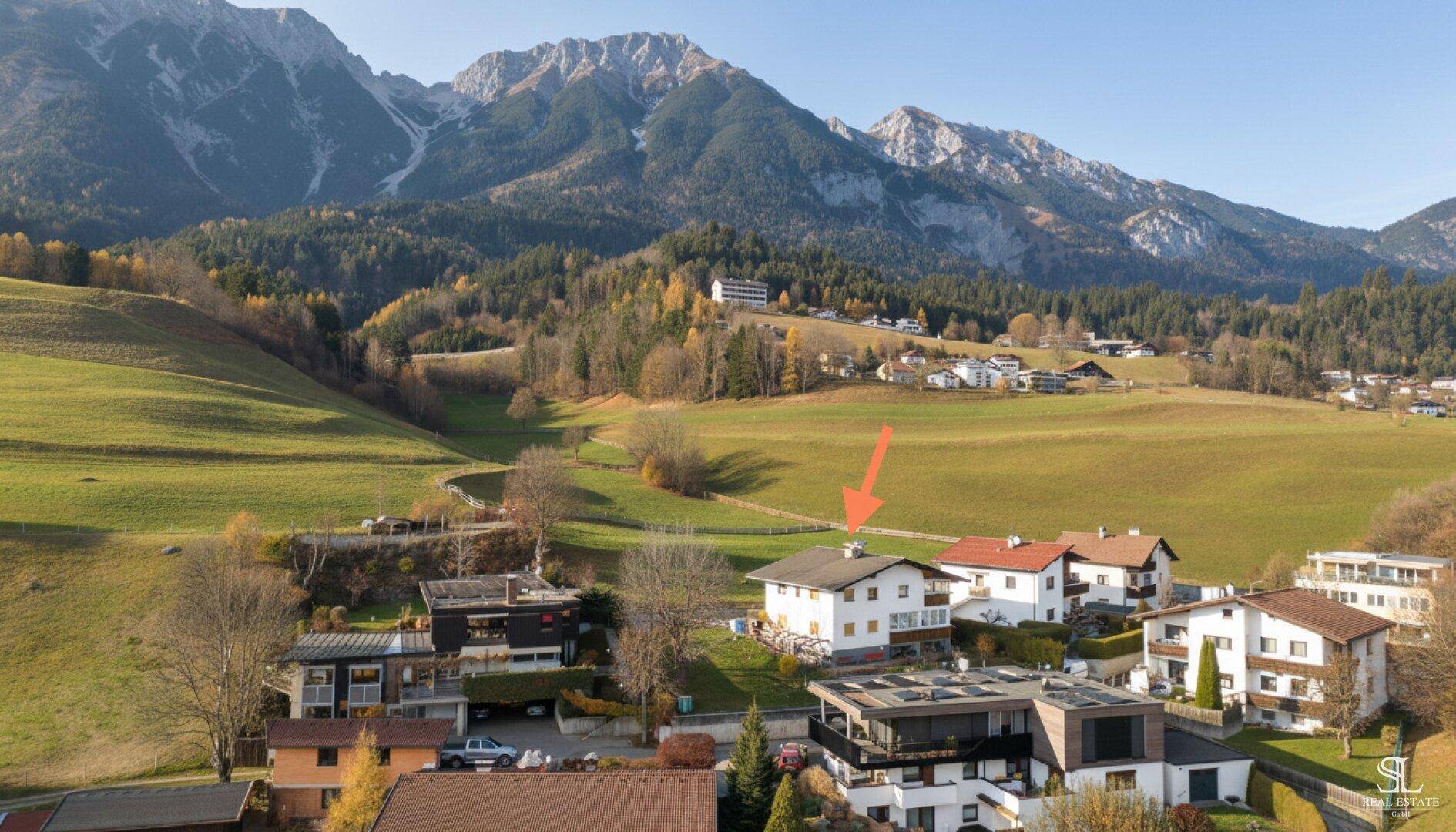 Nahaufnahme des Hauses aus der Vogelperspektive, eingebettet in eine grüne Hügellandschaft mit Bergen im Hintergrund.