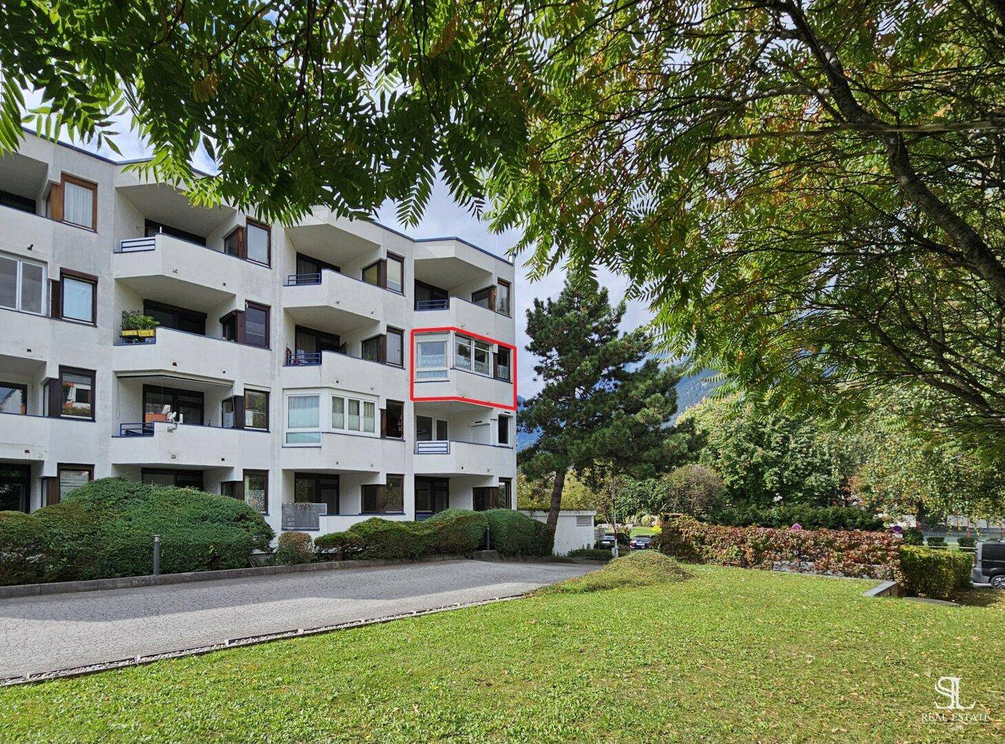 Mehrstöckiges Apartmentgebäude mit Balkonen, umgeben von Bäumen und einer gepflegten Grünfläche.