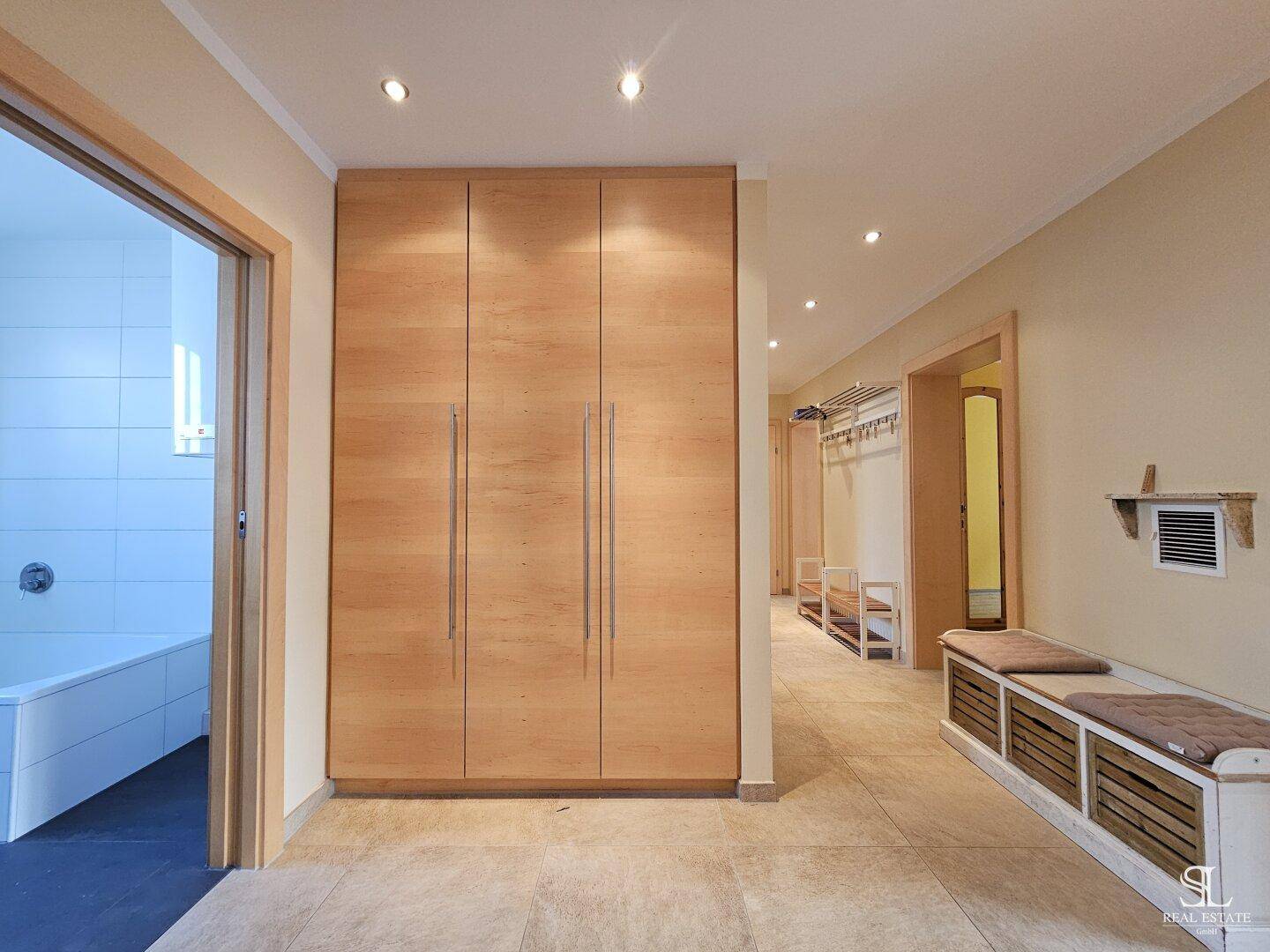 Geräumiger Flur mit Einbauschränken aus Holz, Fliesenboden und praktischer Sitzbank mit Stauraum.