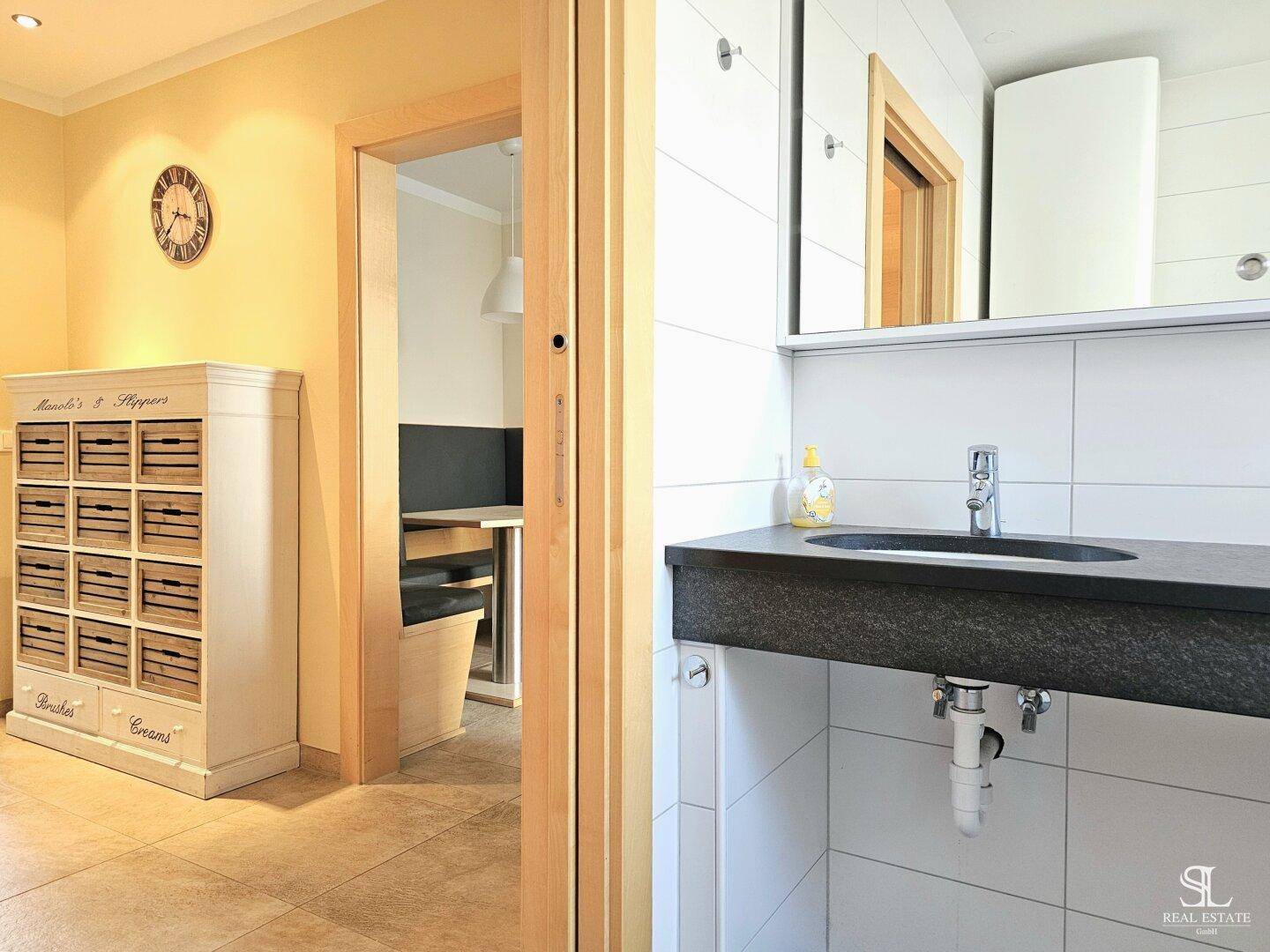 Modernes Badezimmer mit dunklem Waschtisch, Spiegelschrank und Blick in den angrenzenden Flur.
