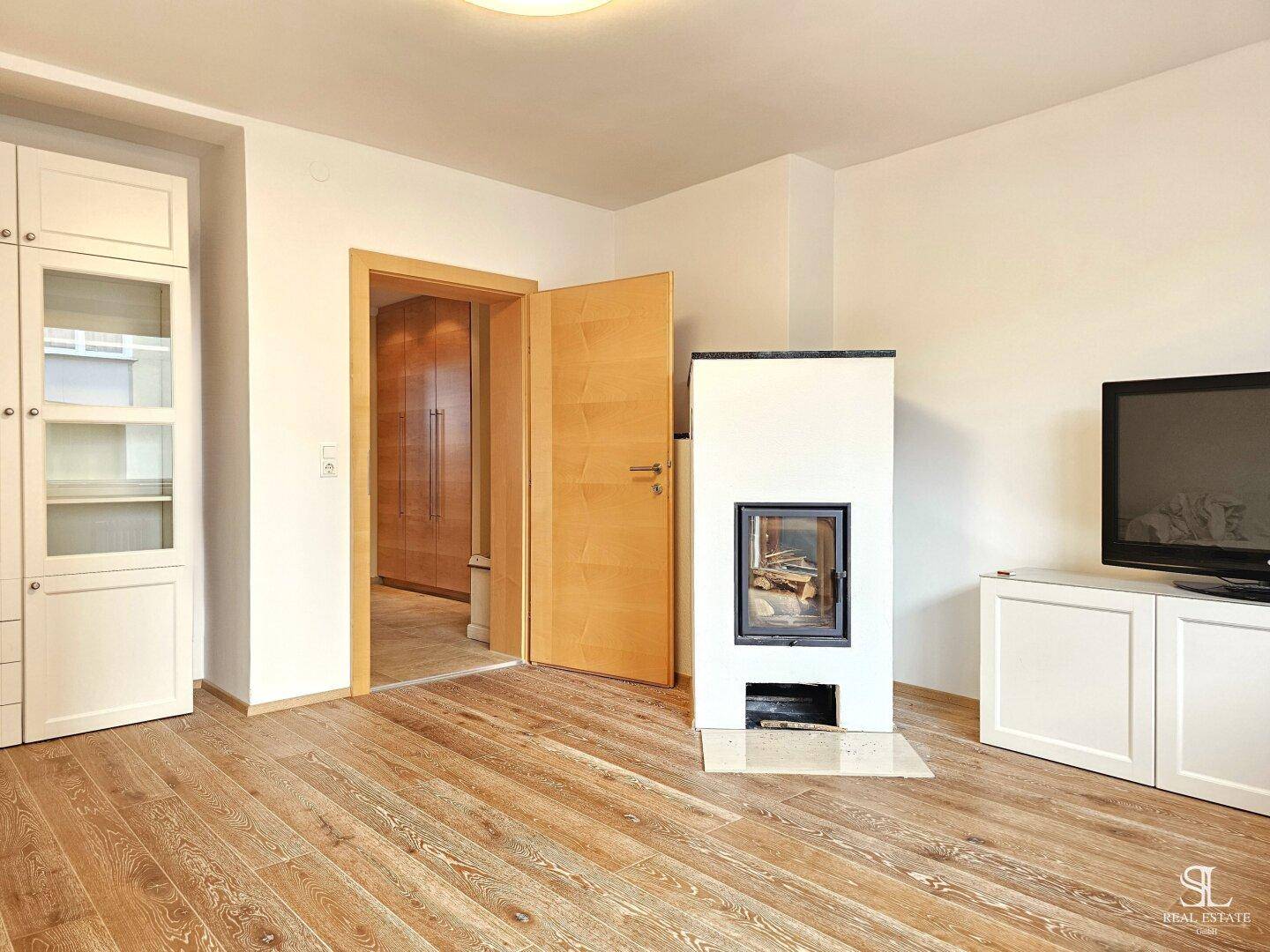 Helles Wohnzimmer mit Holzboden, modernem Kamin und Zugang zu einem weiteren Raum mit Einbauschränken.