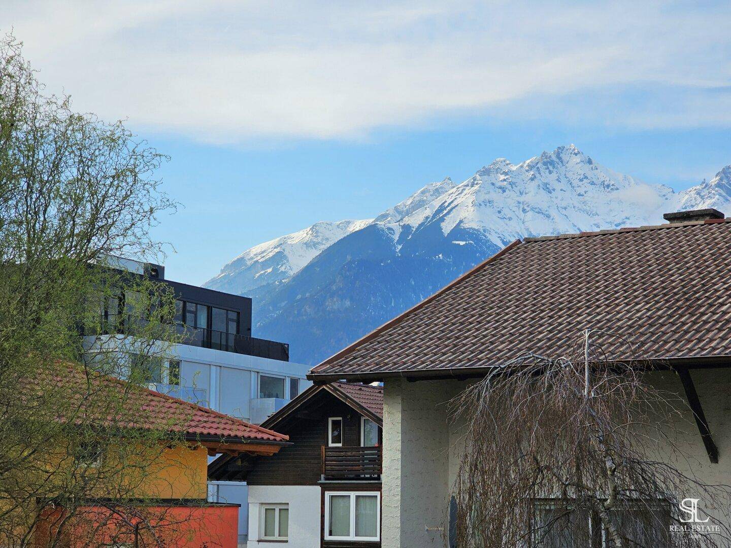 Malerischer Blick auf schneebedeckte Berge über den Dächern der umliegenden Häuser.
