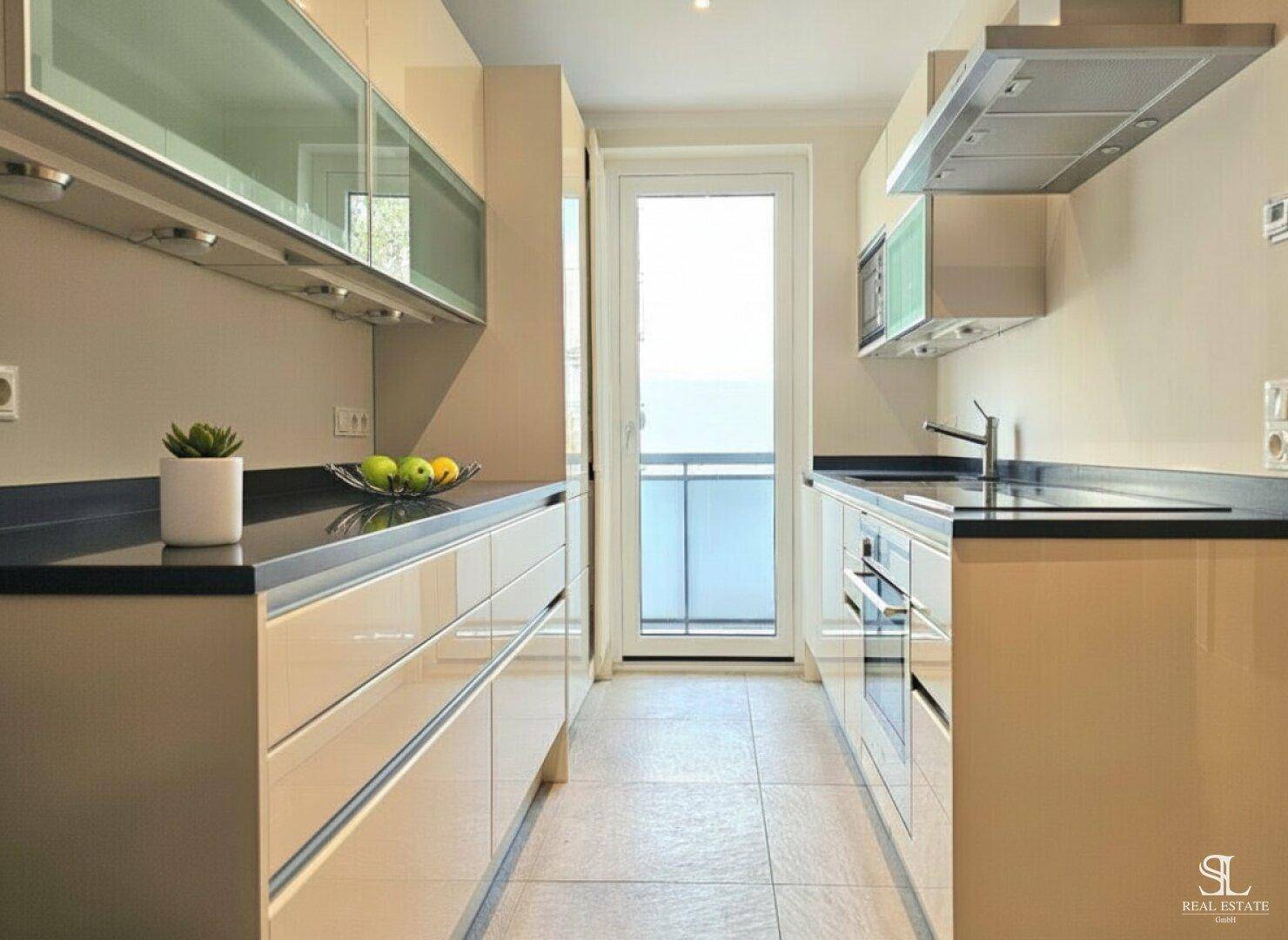 Funktionale Küche mit hellbeigen Schränken, dunklen Arbeitsplatten und Zugang zum Balkon.