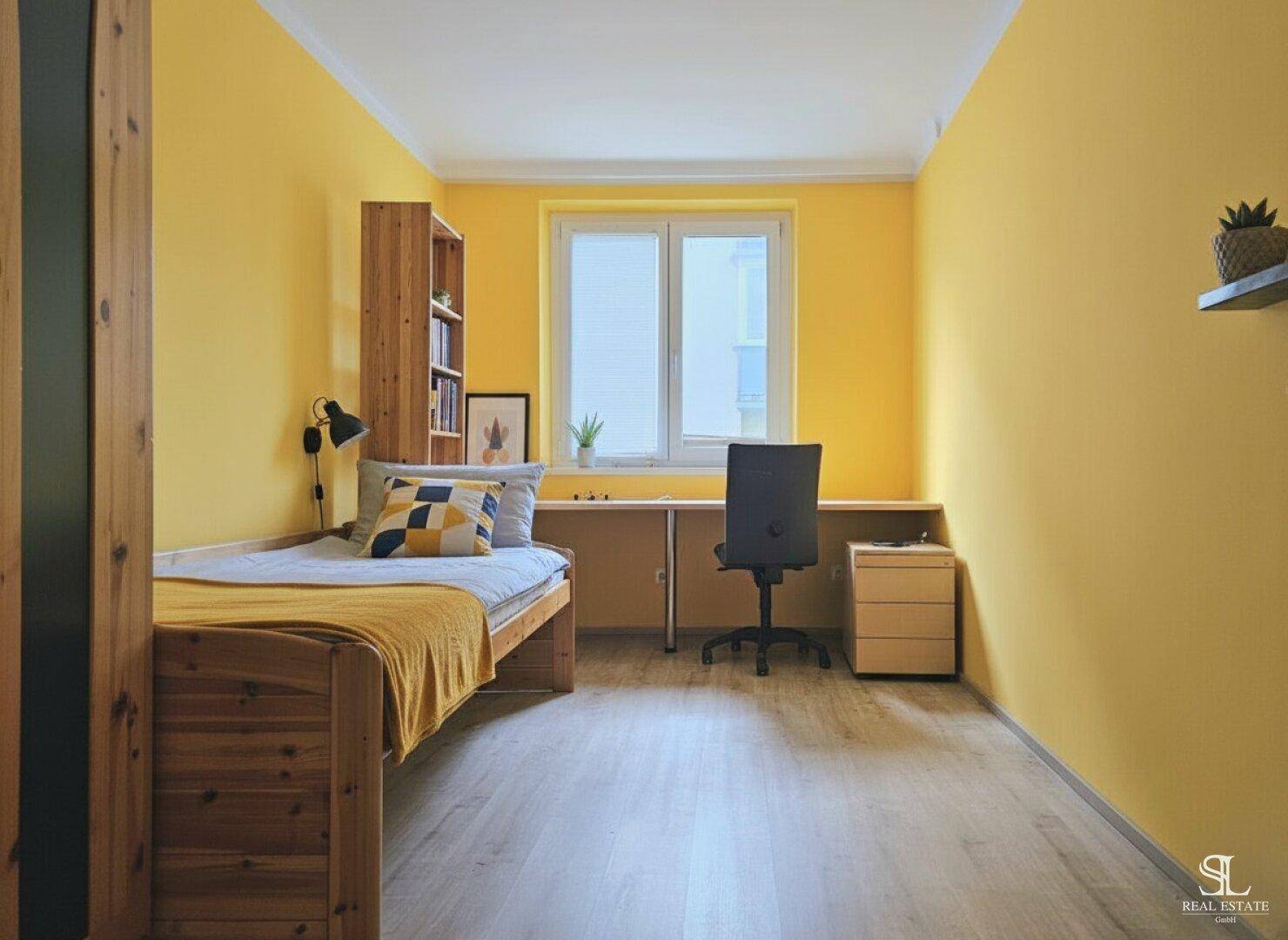 Freundliches Kinderzimmer mit gelben Wänden, Einzelbett und einem langen Schreibtisch unter dem Fenster.