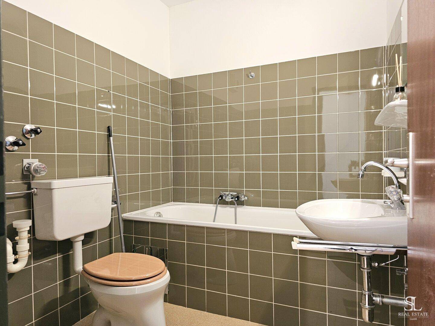Badezimmer mit olivgrünen Fliesen, Badewanne, Toilette und Waschbecken in klassischem Stil.