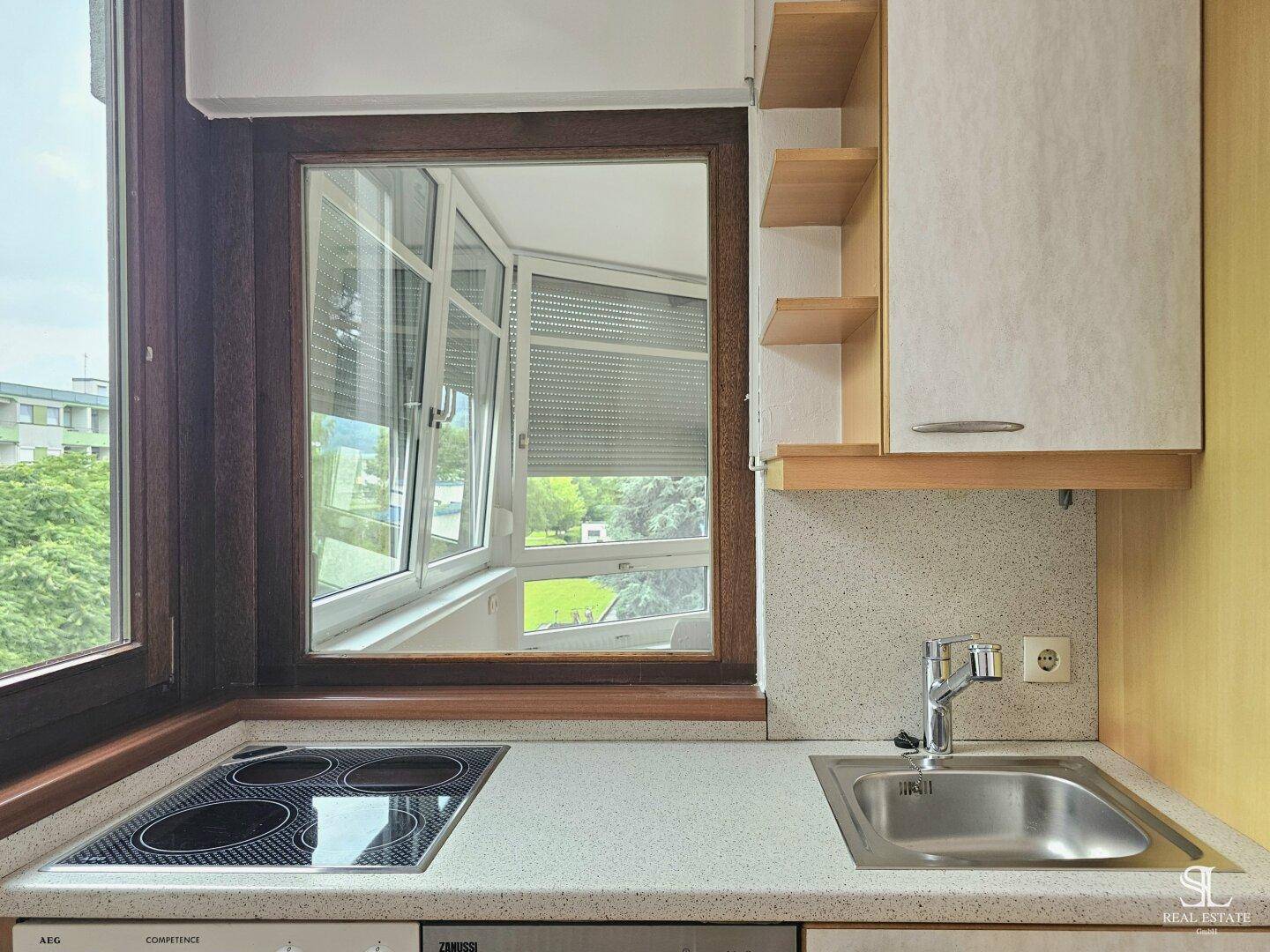 Küchenzeile mit Spüle, Elektrokochfeld und Fenster, das einen Blick nach draußen ermöglicht.