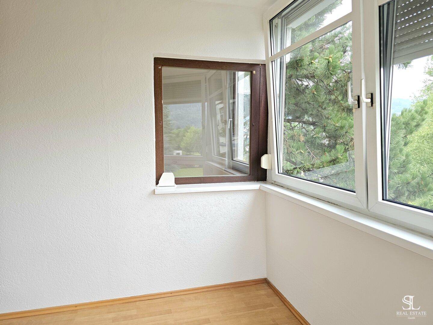 Heller Raum mit Fenster, das einen Blick auf grüne Bäume und die Umgebung freigibt.
