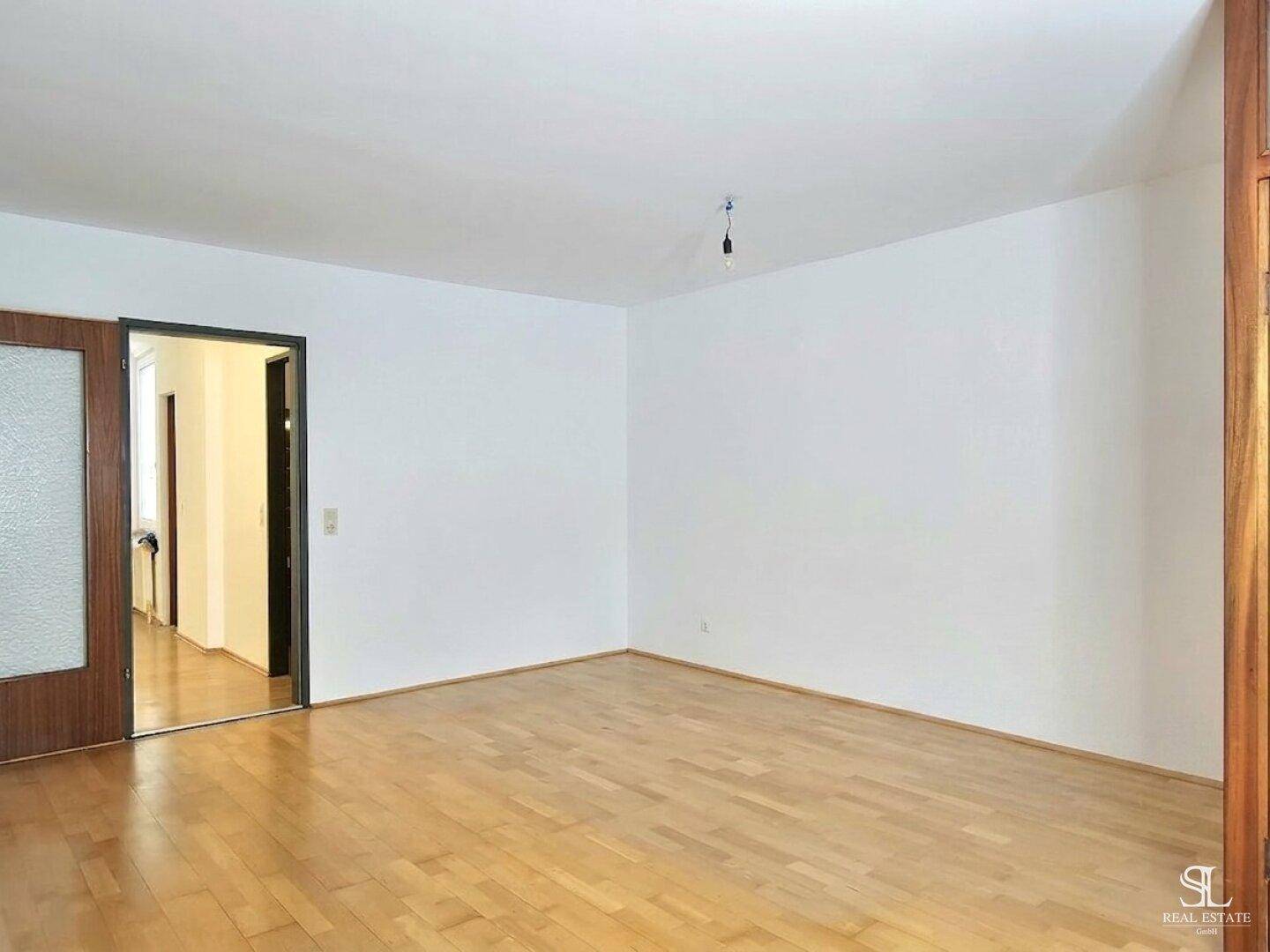 Geräumiger, leerer Raum mit Holzboden und Zugang zu einem Flur, ideal zur individuellen Gestaltung.