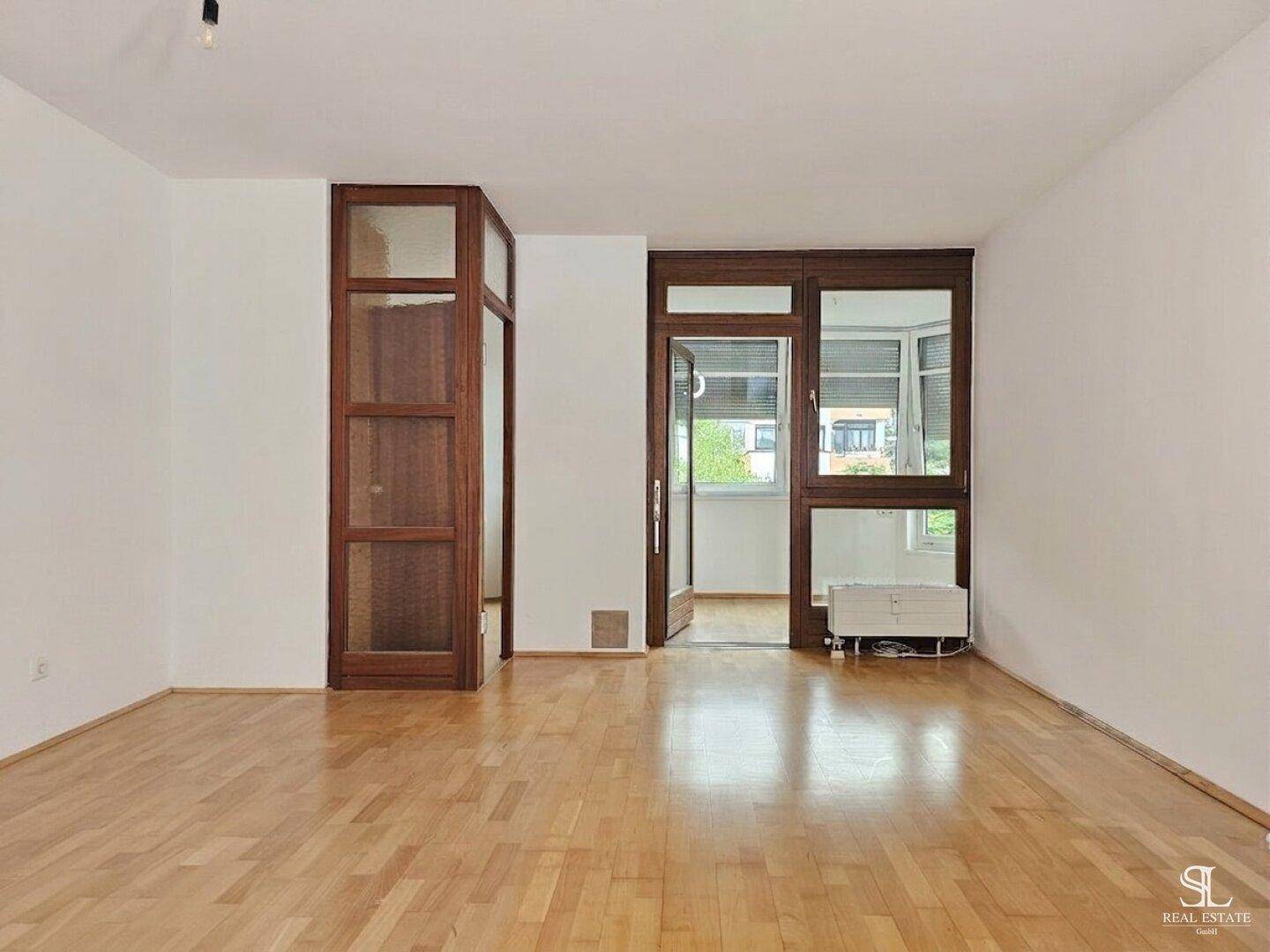 Heller, leerer Raum mit Holzboden und großzügiger Fensterfront, die viel Tageslicht hereinlässt.