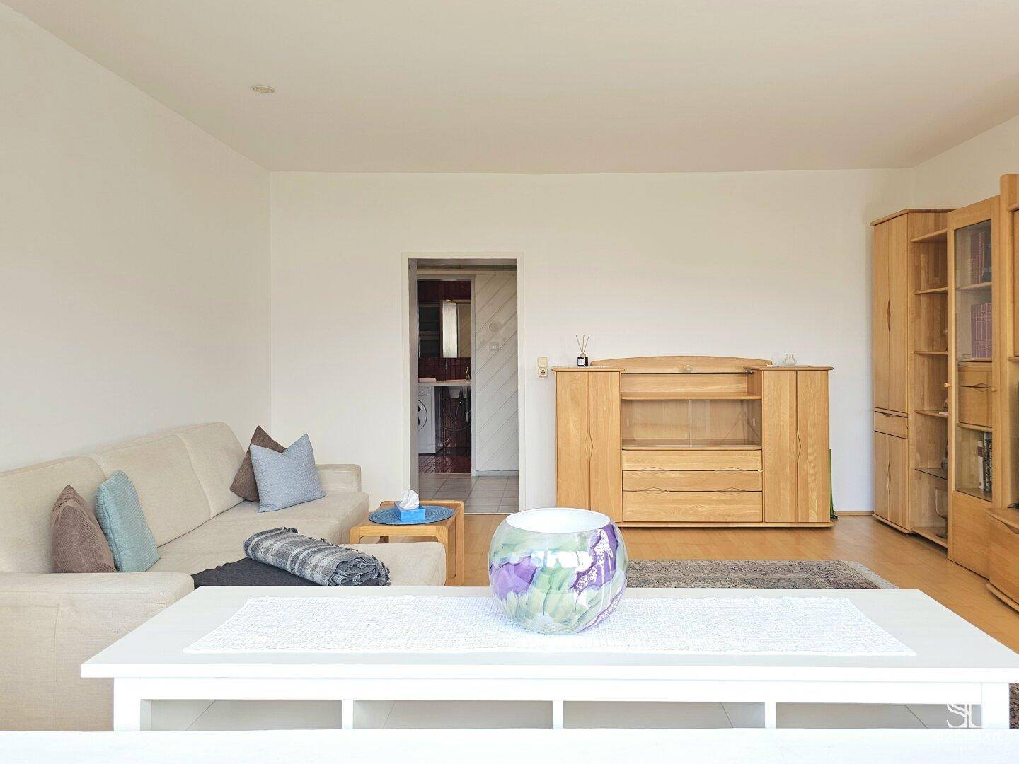 Wohnzimmer mit Sofa und Holzmöbeln, das zu einem weiteren Raum führt.