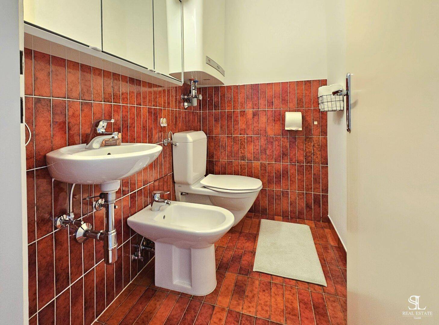 Kleines Badezimmer mit orange-braunen Fliesen, Waschbecken, Toilette und Bidet.