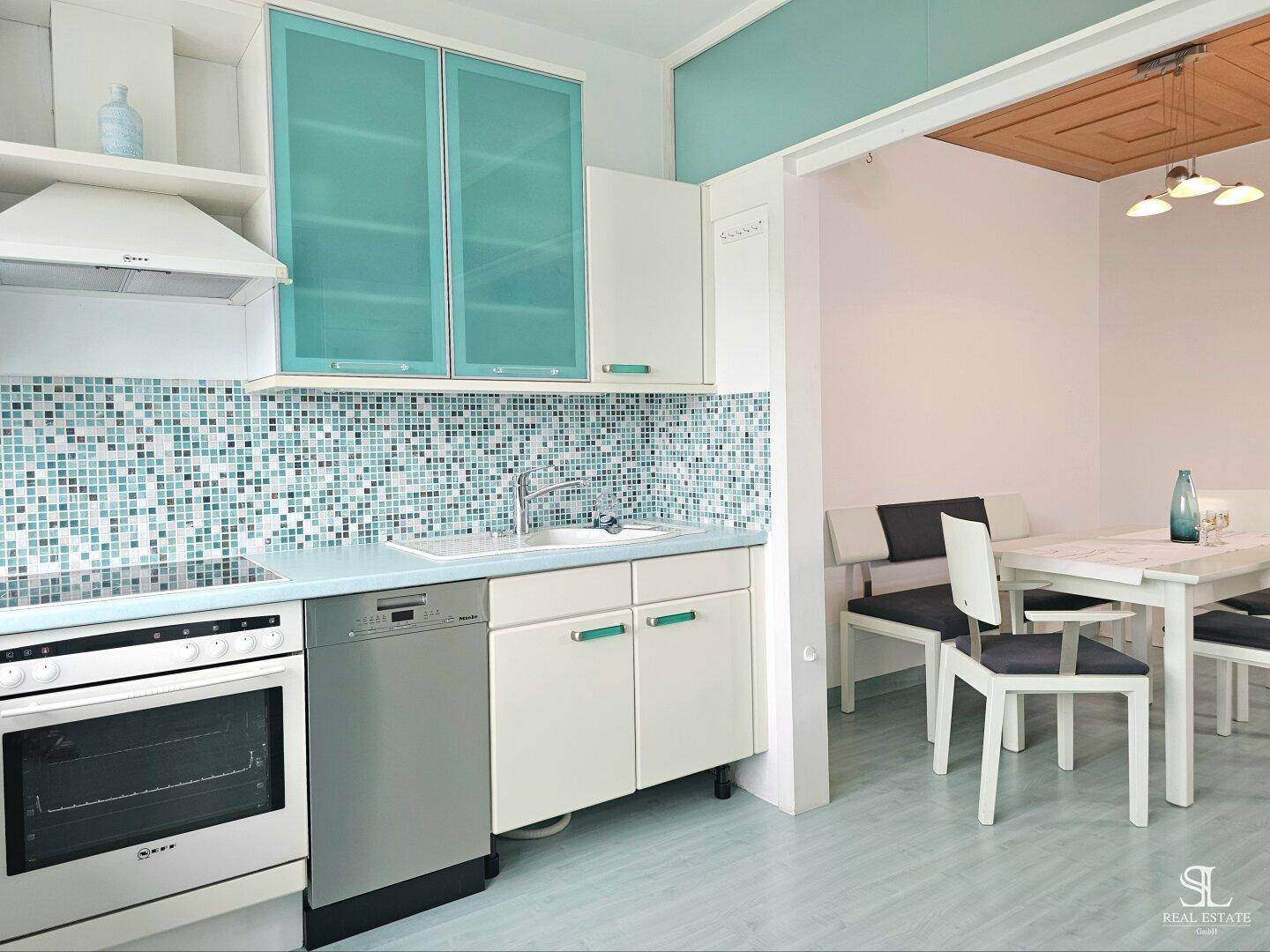 Küche mit türkisfarbenen Schränken und Mosaikfliesen, offen zum Essbereich.