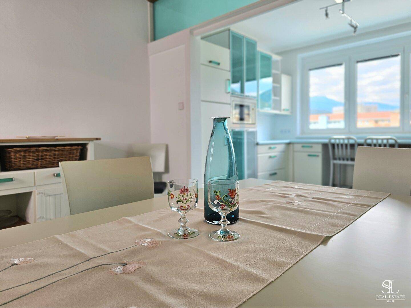 Essbereich mit weißem Tisch und Stühlen, offen zur Küche, mit Holzakzenten an der Decke.