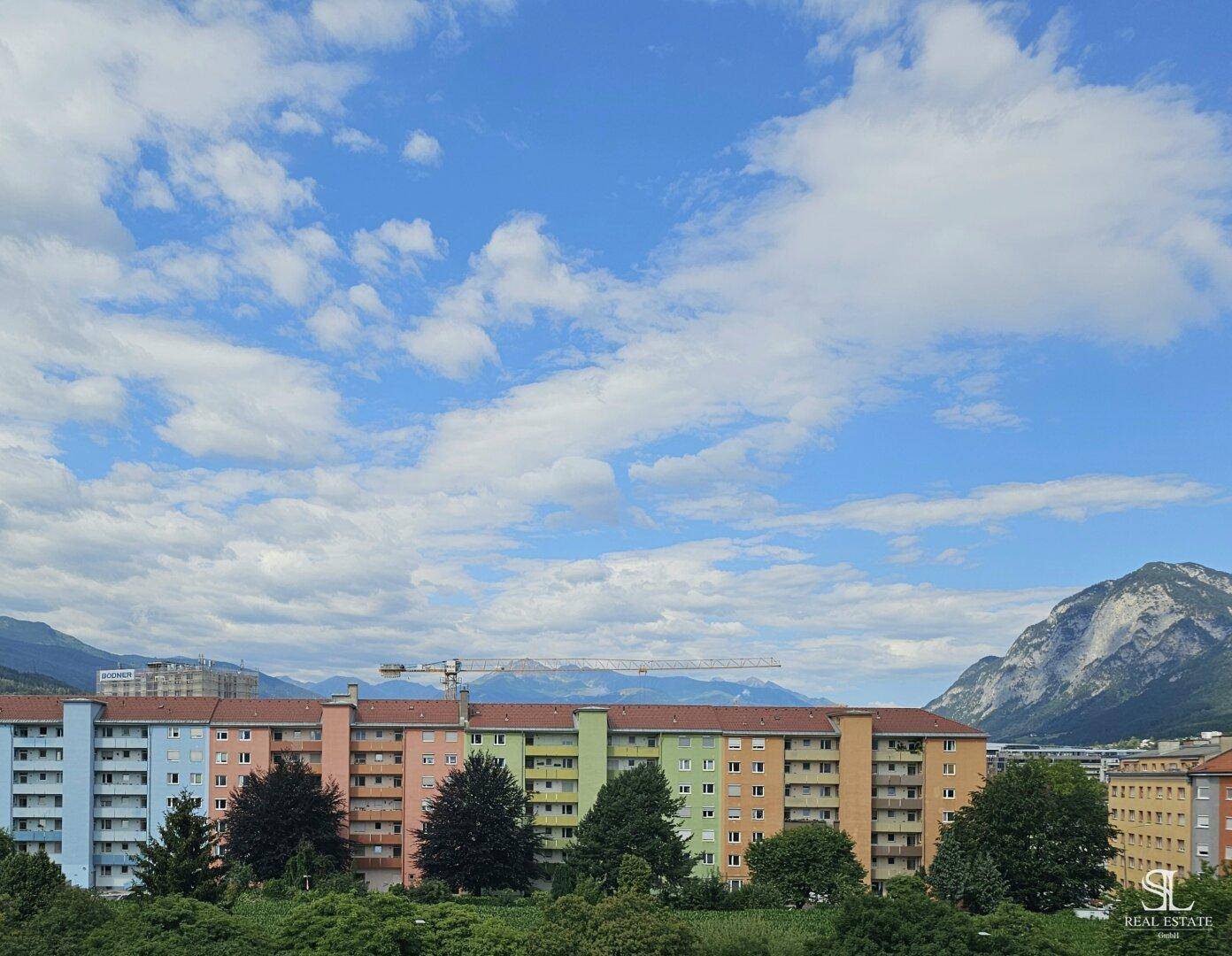 Weitläufiger Blick auf die Stadt und die umliegende Berglandschaft unter blauem Himmel.