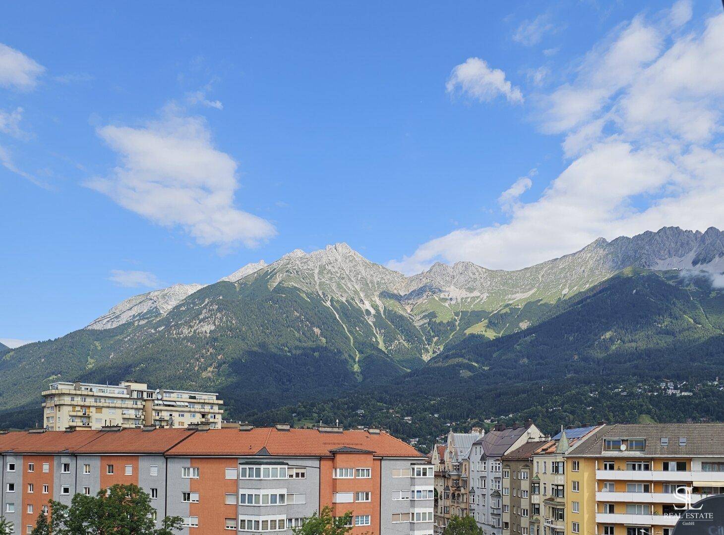 Atemberaubender Panoramablick auf schneebedeckte Berge und städtische Gebäude unter blauem Himmel.