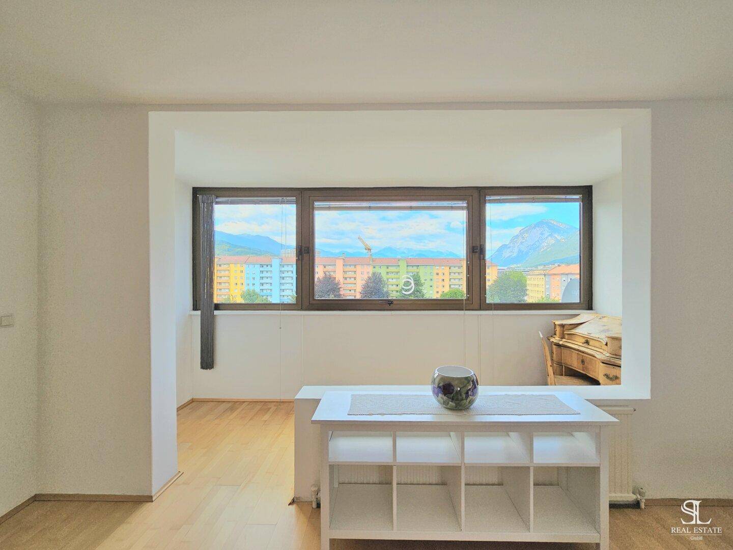 Heller Wohnbereich mit Parkettboden und einem breiten Fenster, das einen weiten Blick bietet.
