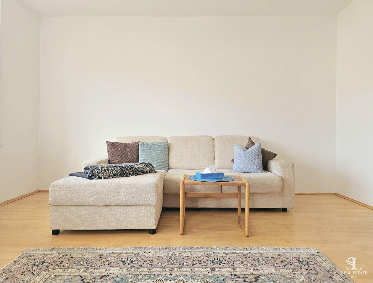 Schlichtes Wohnzimmer mit beigem Sofa und Teppich, ideal für entspannte Stunden.