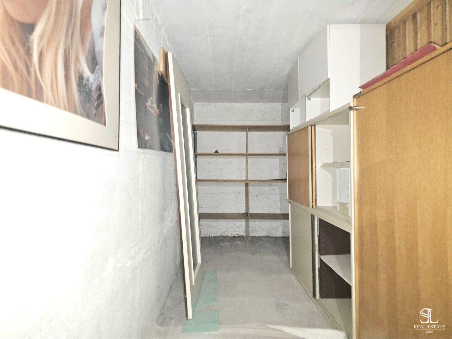 Einfacher Kellerraum mit Betonwänden, Regalen und Stauraum für verschiedene Gegenstände.