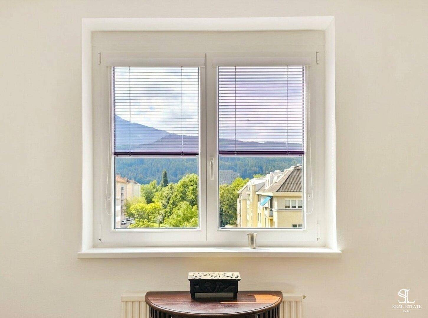 Fenster mit Jalousien bietet einen malerischen Blick auf Berge und umliegende Gebäude.