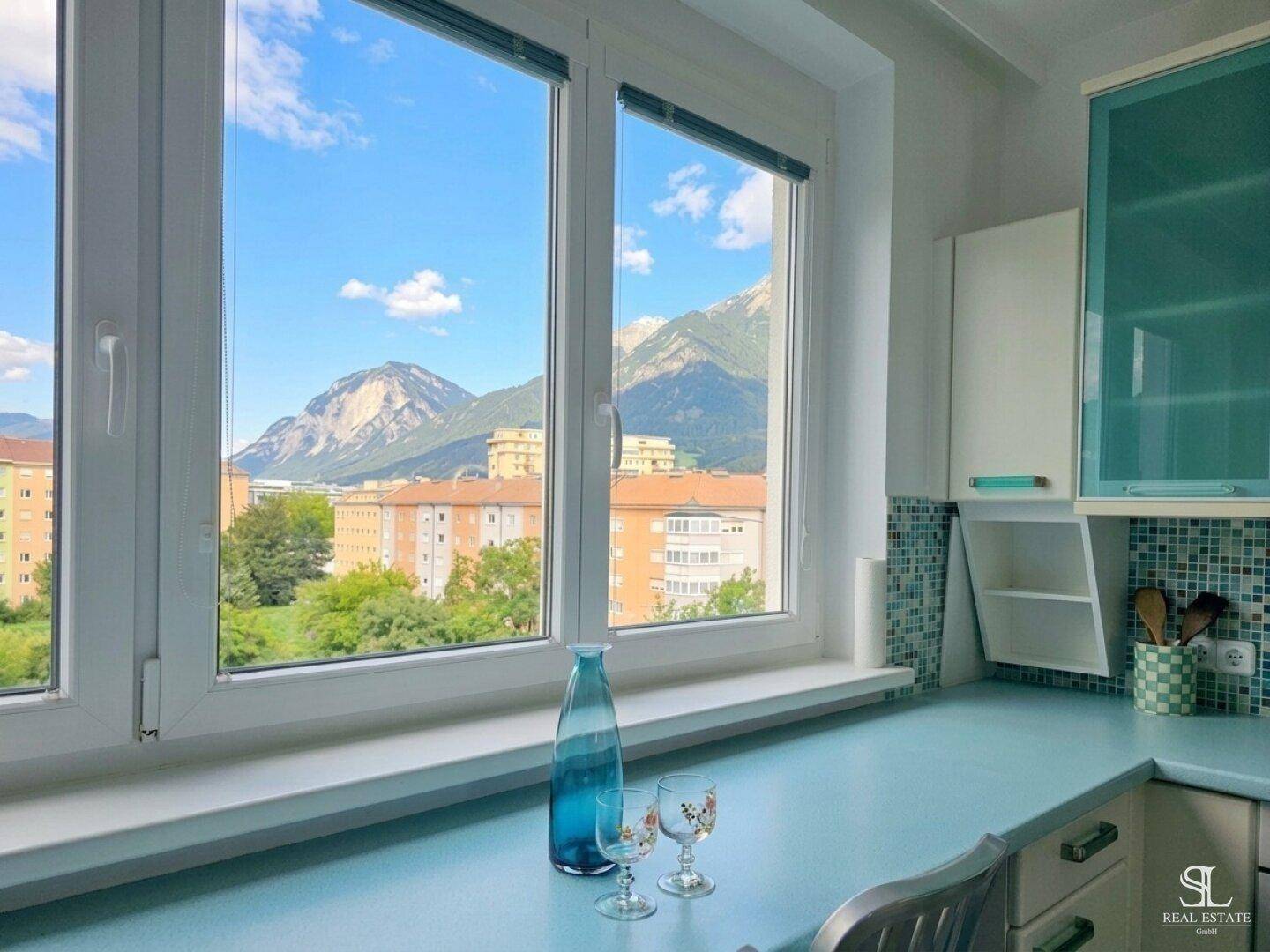 Heller Küchenbereich mit türkisfarbener Arbeitsplatte und beeindruckendem Bergblick durch große Fenster.